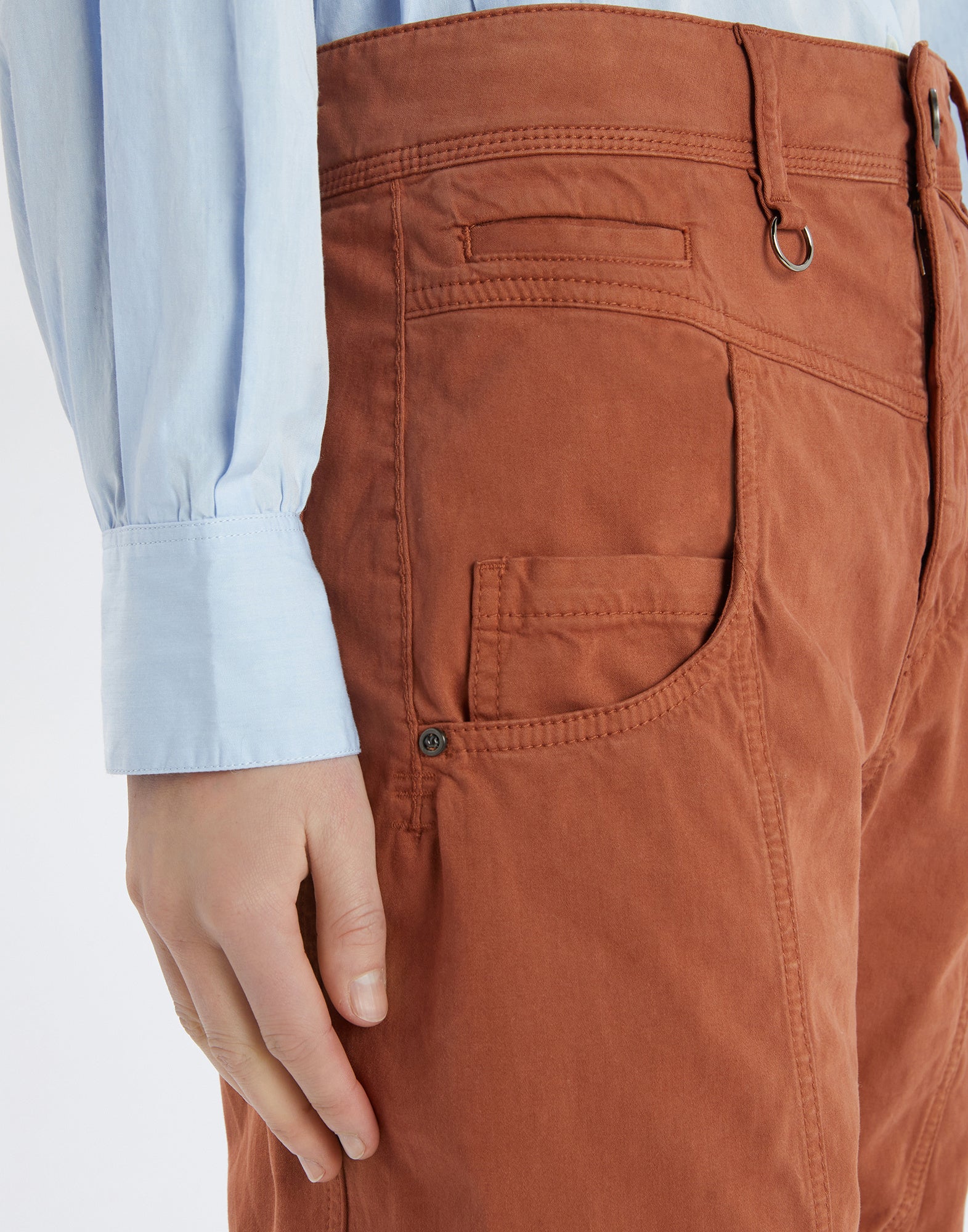 Detailansicht der Hose FURORE: Nahaufnahme zeigt rostbraunen Stoff, sichtbare Nähte, aufgesetzte Taschen, Gürtelschlaufe und Metallring an der Taille.