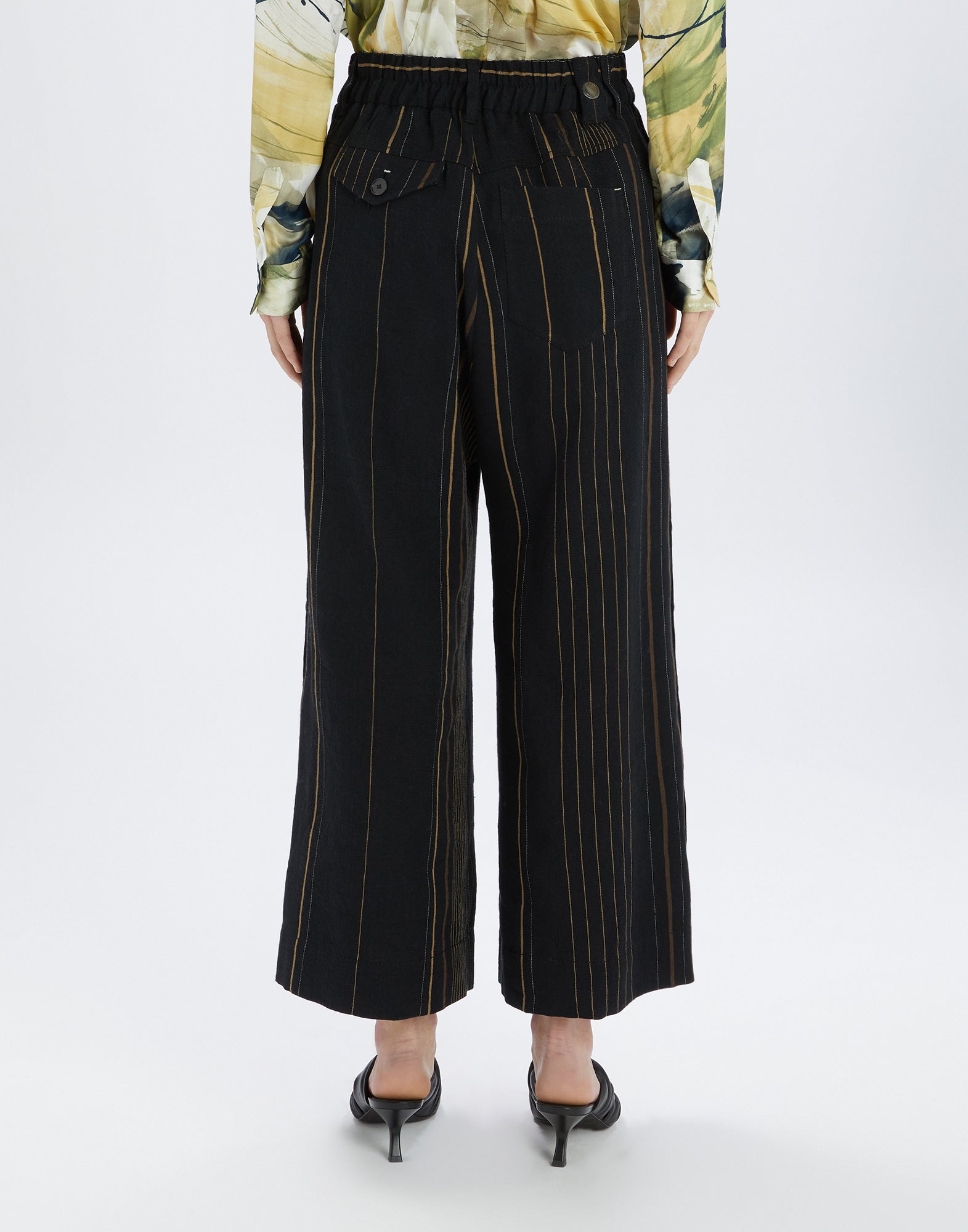 Rückansicht der SWALLOW Hose, knöchellang aus schwarzem Stoff mit farbigen vertikalen Streifen, einer Knopfleiste und Gesäßtaschen mit Leiste und Patte.