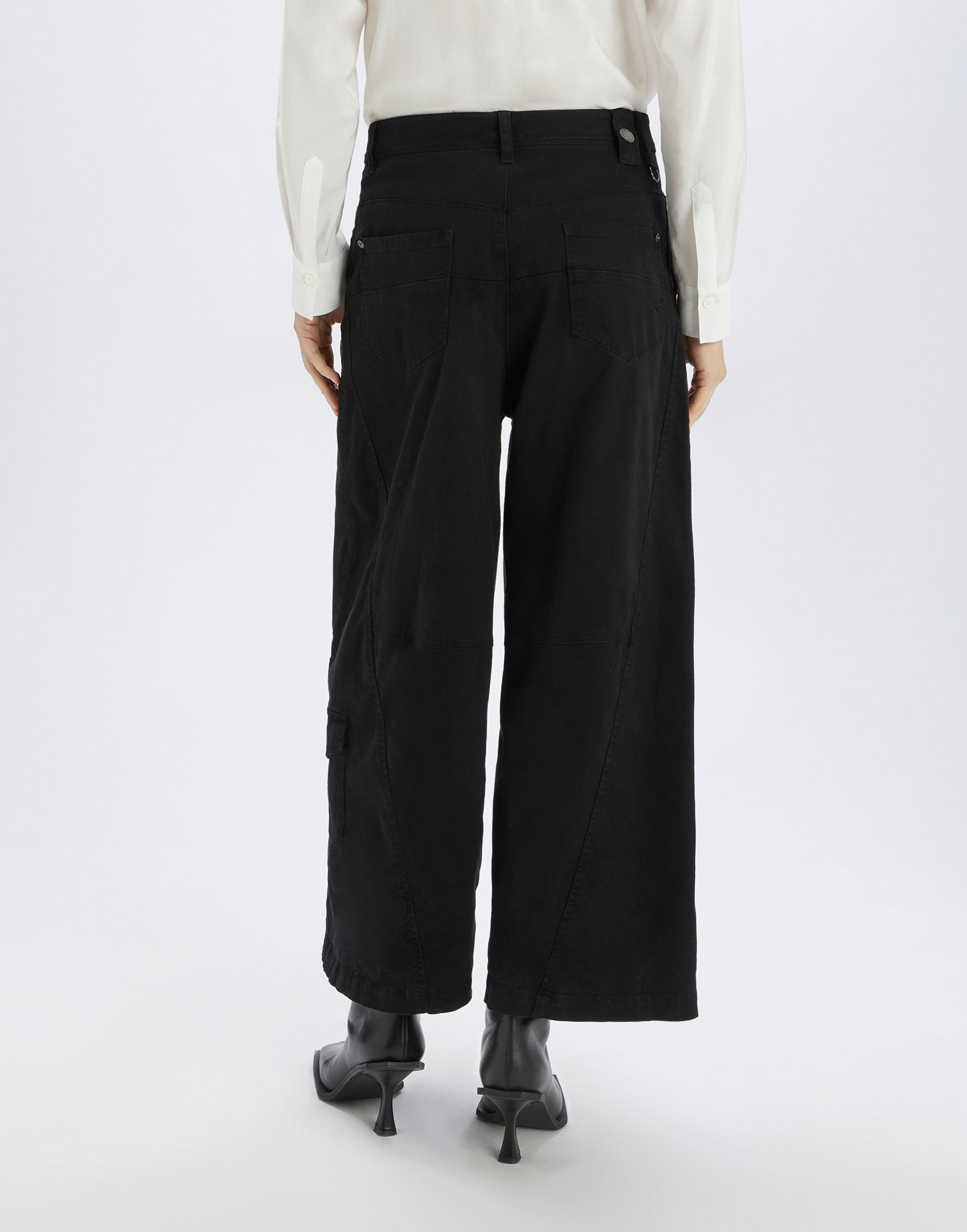 Rückansicht der Hose OUT RUN zeigt eine weite Silhouette ab der Hüfte, zwei aufgesetzte Gesäßtaschen und markante Steppnähte, getragen mit Absatzschuhen.