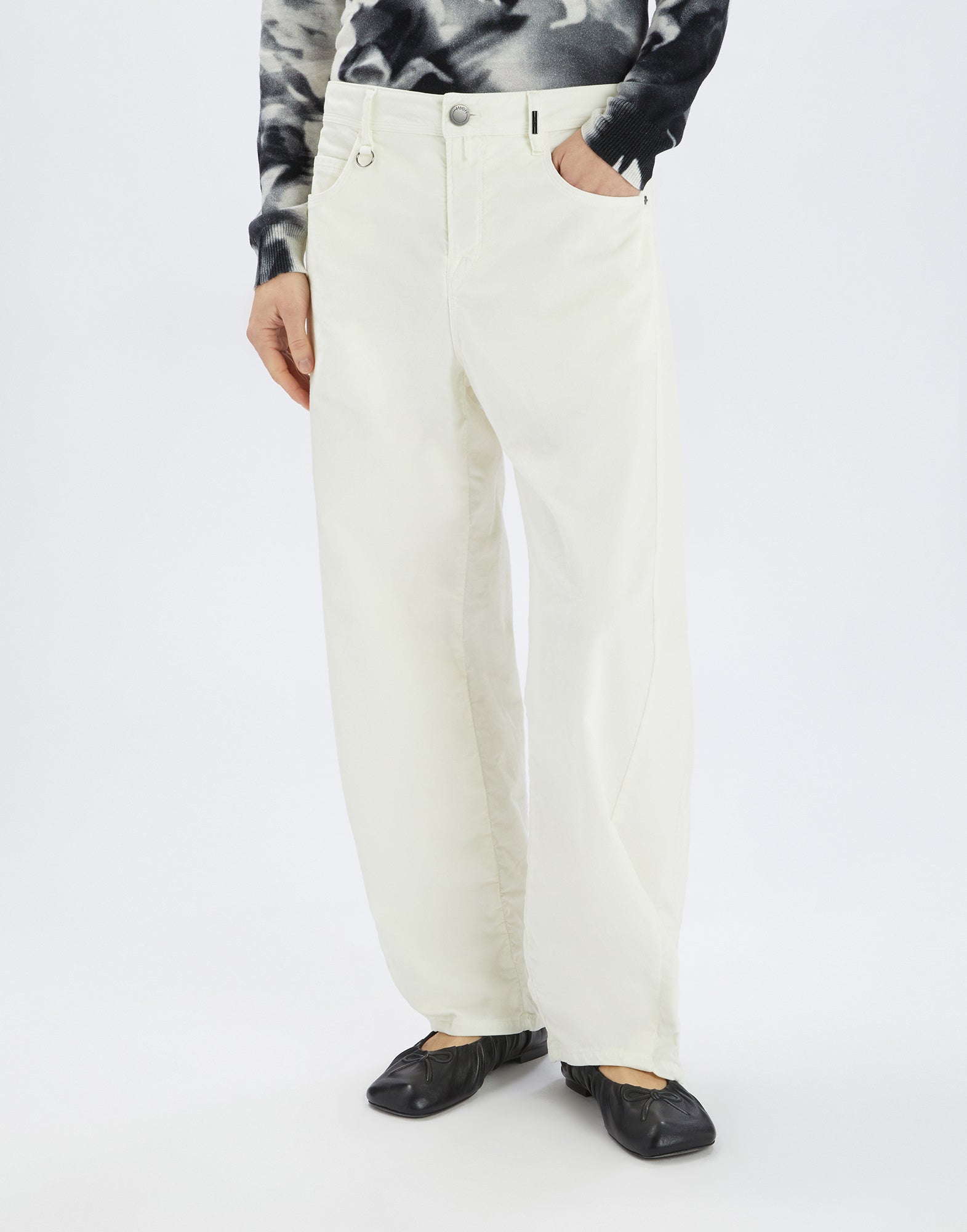 Front view: Person wearing the GOTLAND trousers in light off-white, featuring wide legs, front pockets, visible seams, and front button, urban-chic style.