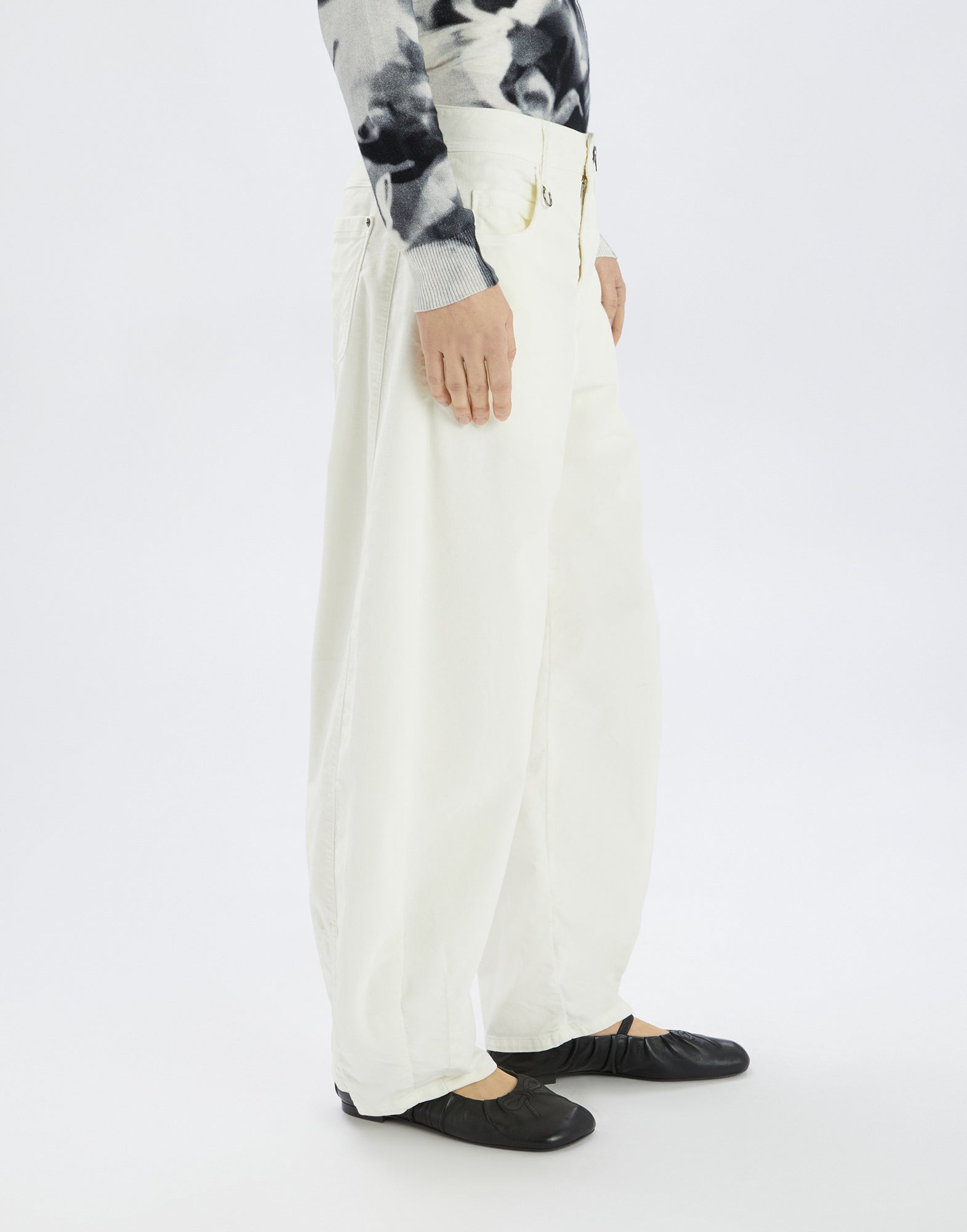 Side view of the white, wide GOTLAND trousers featuring a visible zipper and waistband, worn by a person with black shoe.