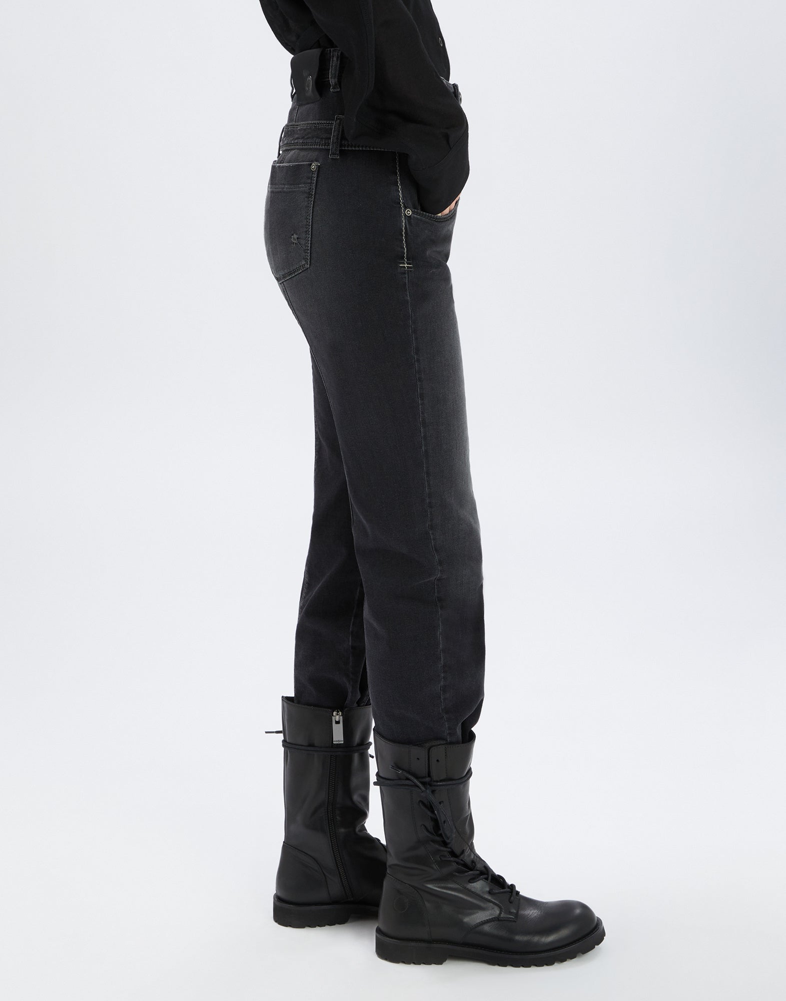 Side view of FAIR-PLAY classic black jeans with slightly elastic slim fit, removable double belt, and visible seams, worn with black boots.