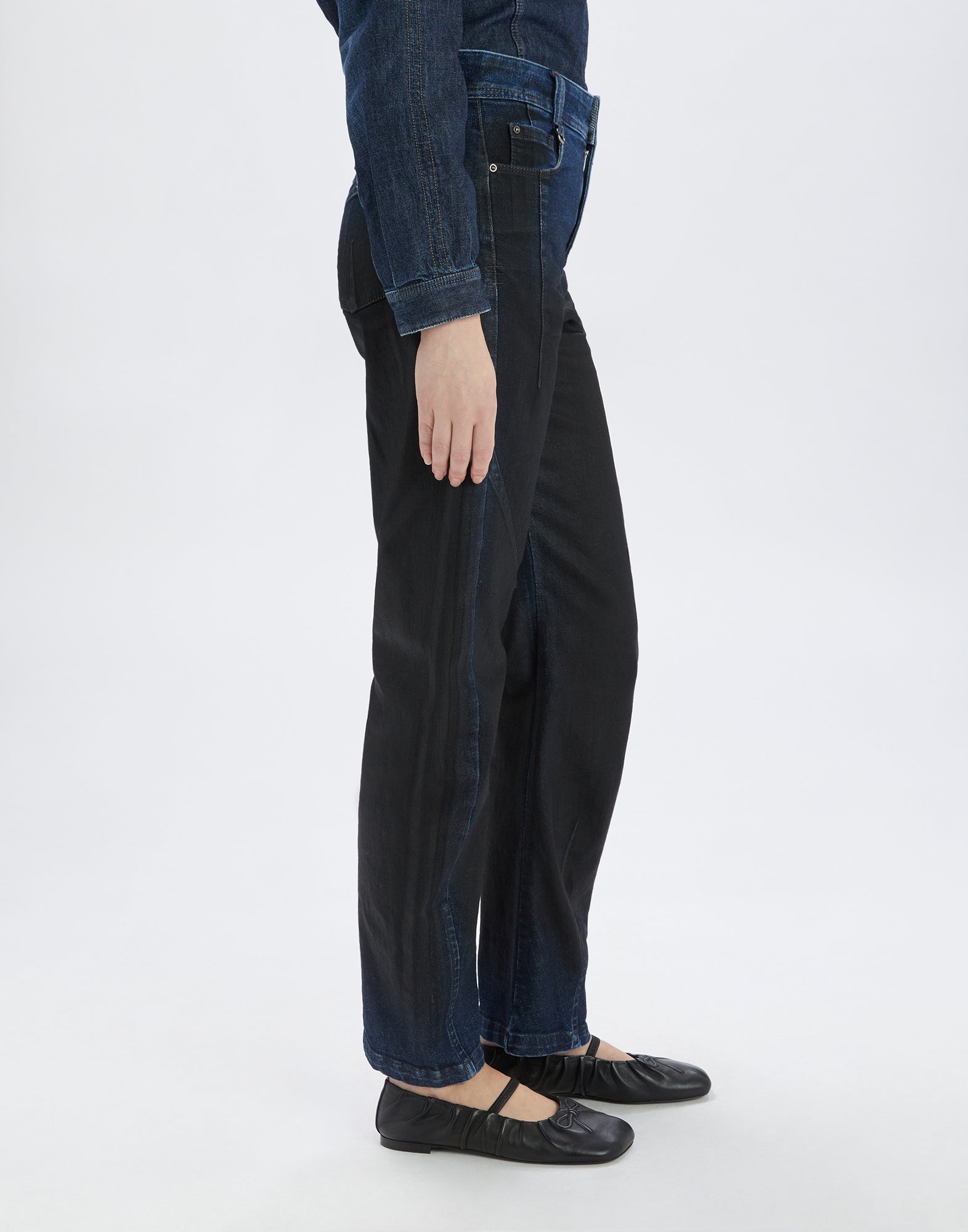 Seitenansicht einer Person mit der Jeans TRICE, gerade geschnitten, dunkler Denim mit leichter Bananenform, sichtbare Nähte und Falten am Knie.