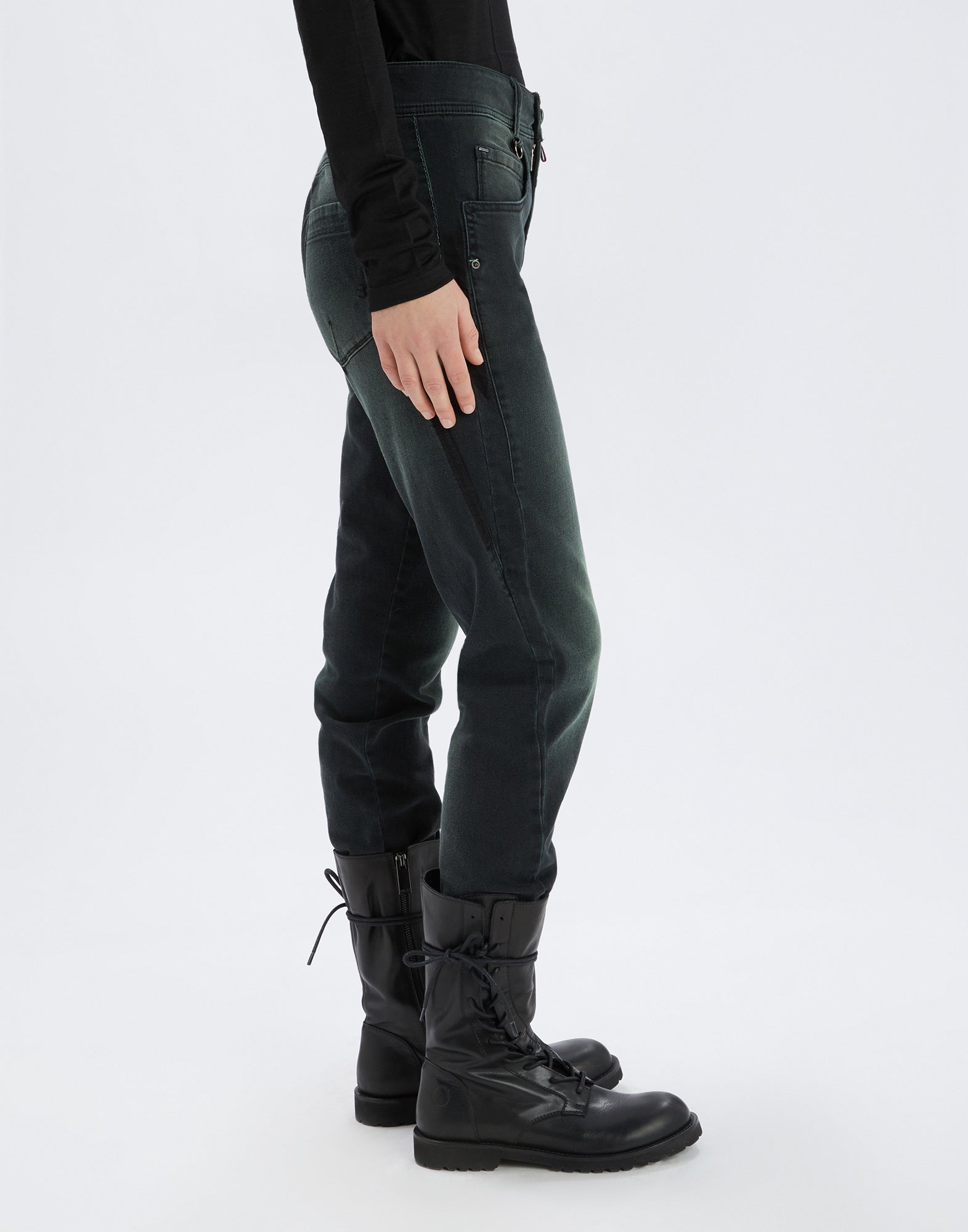 Side view of HAPPLY jeans worn with black boots. Visible darker panels, back patch pockets, stretch denim, and waistband with belt loops.