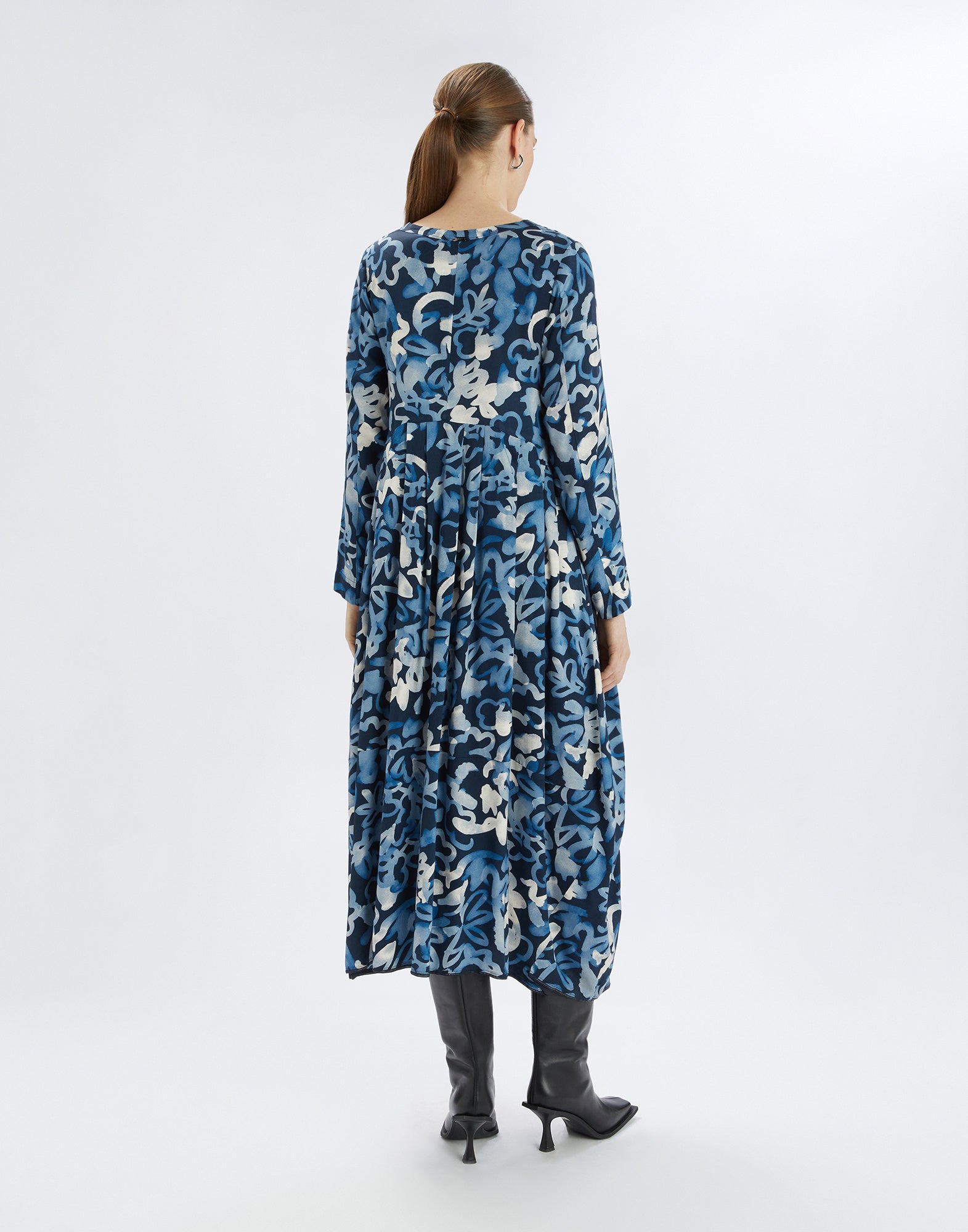 Rear view of the structured AWAKENING dress with balloon skirt and vibrant electric blue print, worn by a woman with boots.