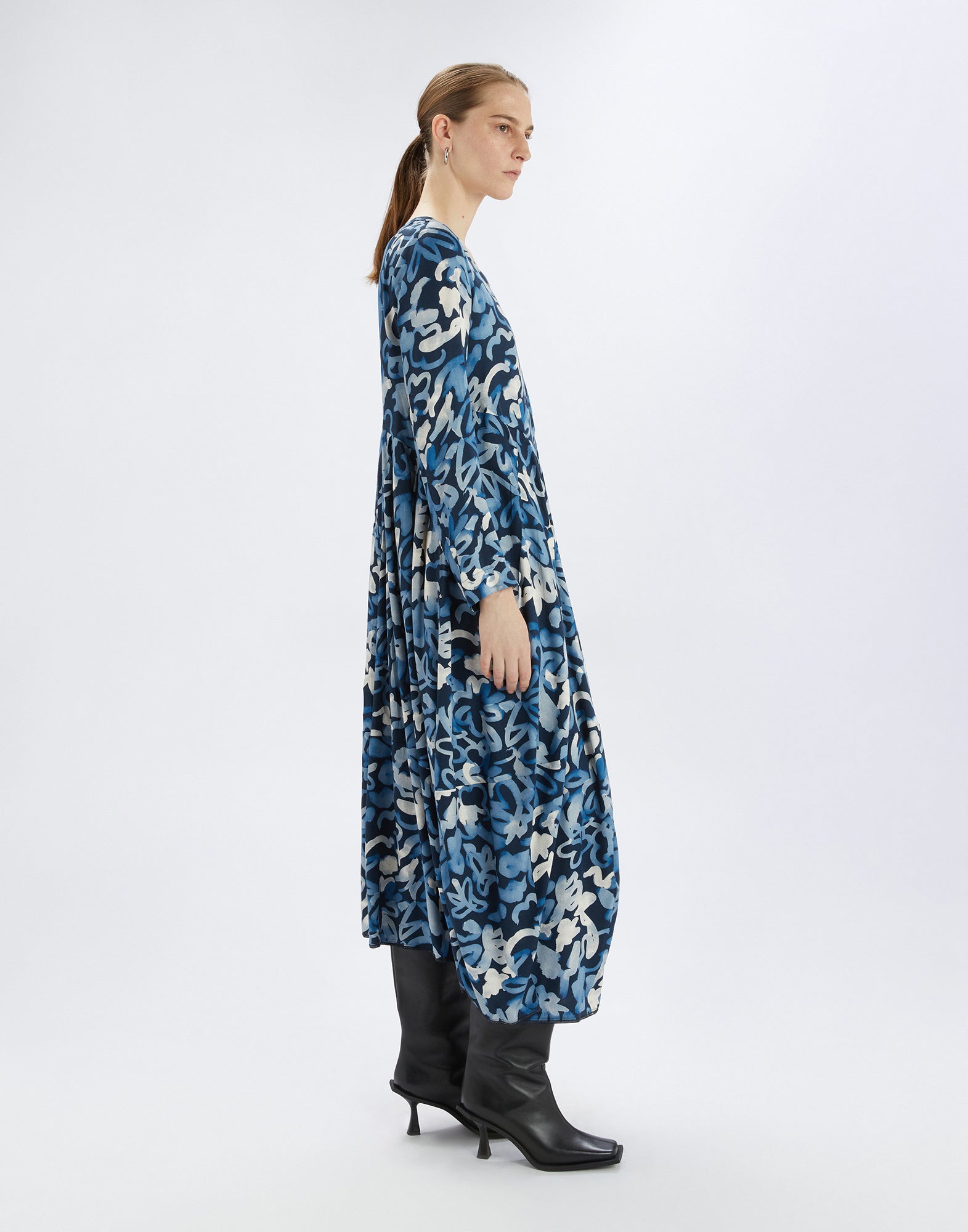 Side view of a model in the AWAKENING dress with vibrant electric blue pattern, balloon skirt, and fitted bodice, paired with black boots.