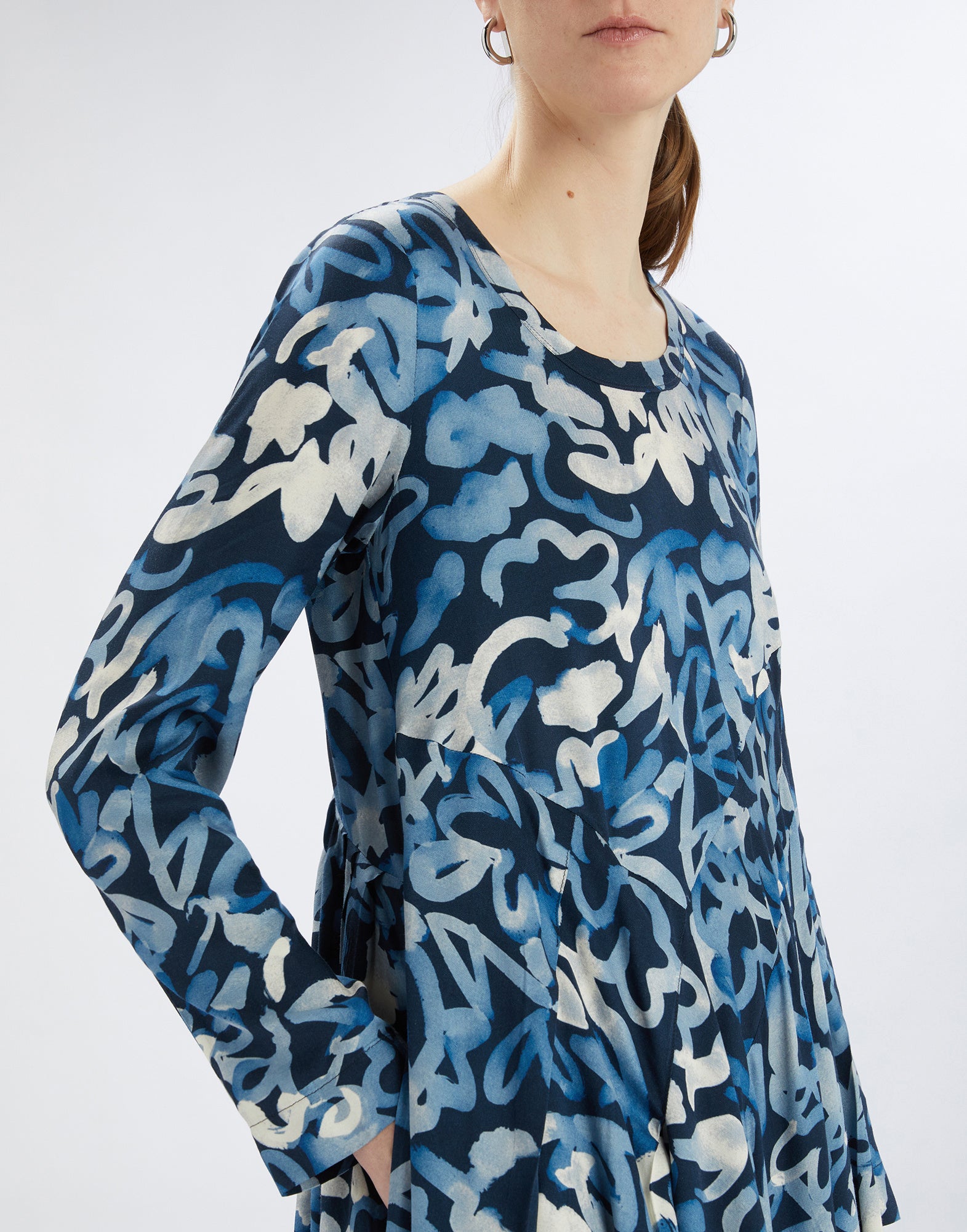 Front view: Model wears AWAKENING dress with vibrant electric blue abstract pattern, round neckline, three-quarter sleeves, and fitted bodice.