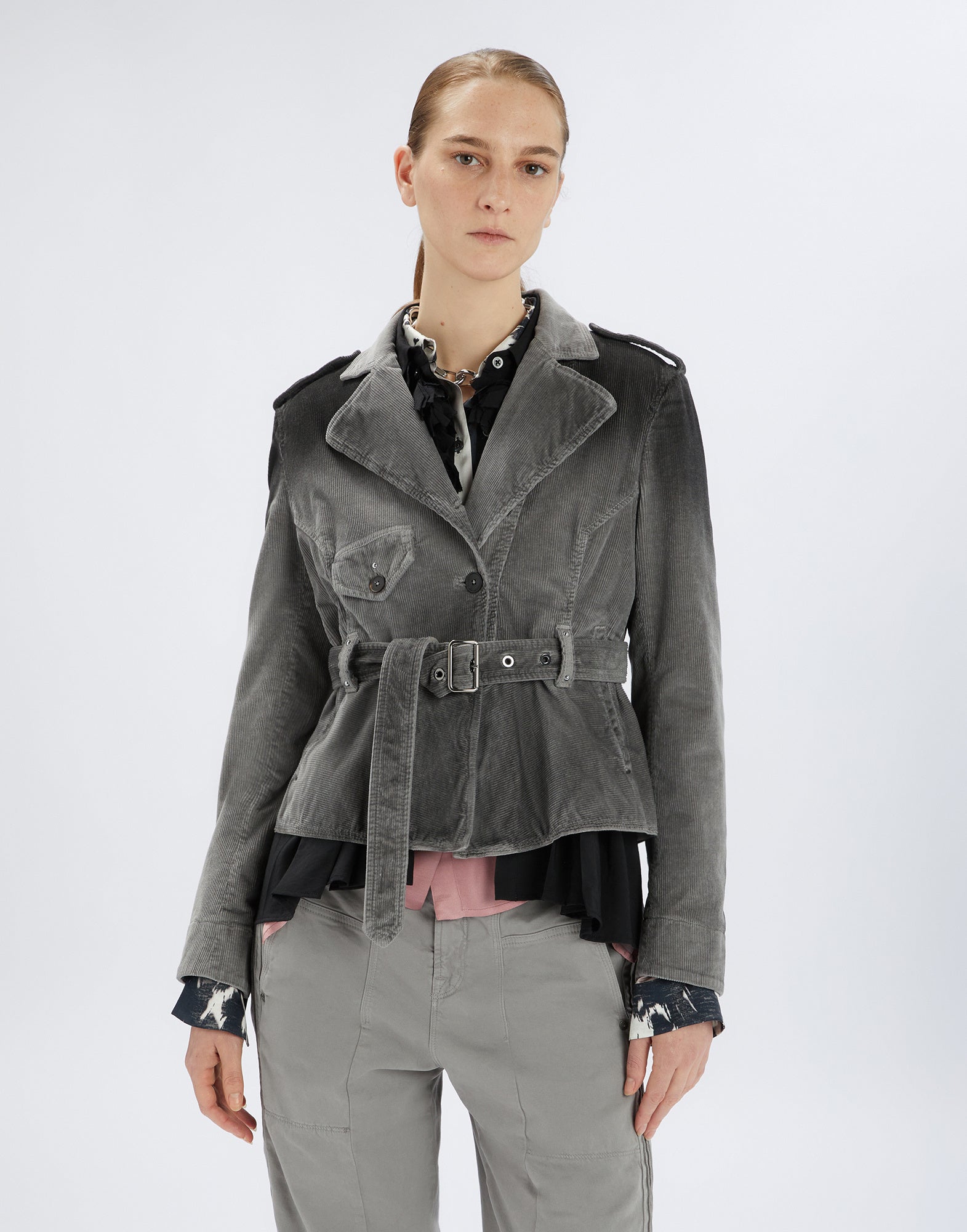 Front view: woman wears GIG biker jacket in grey corduroy with wide lapels, double-breasted buttons, chest pocket, belt, and exposed stitching.