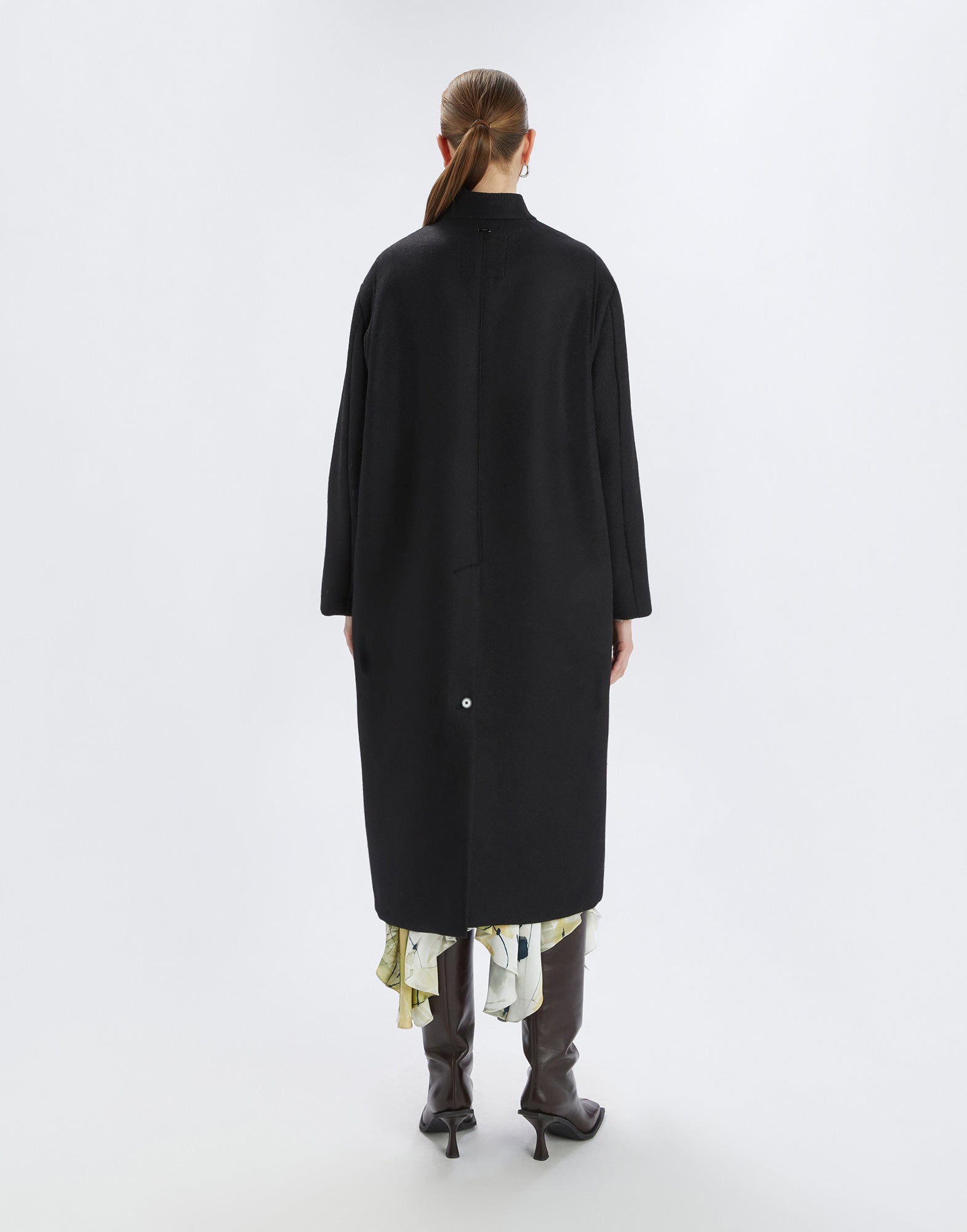 Rückansicht: Person trägt den PANTO Mantel in Schwarz, knöchellang mit Oversize-Passform, rückseitigem Maxi-Schlitz mit Knopf und Stehkragen, städtisch-elegantes Design.