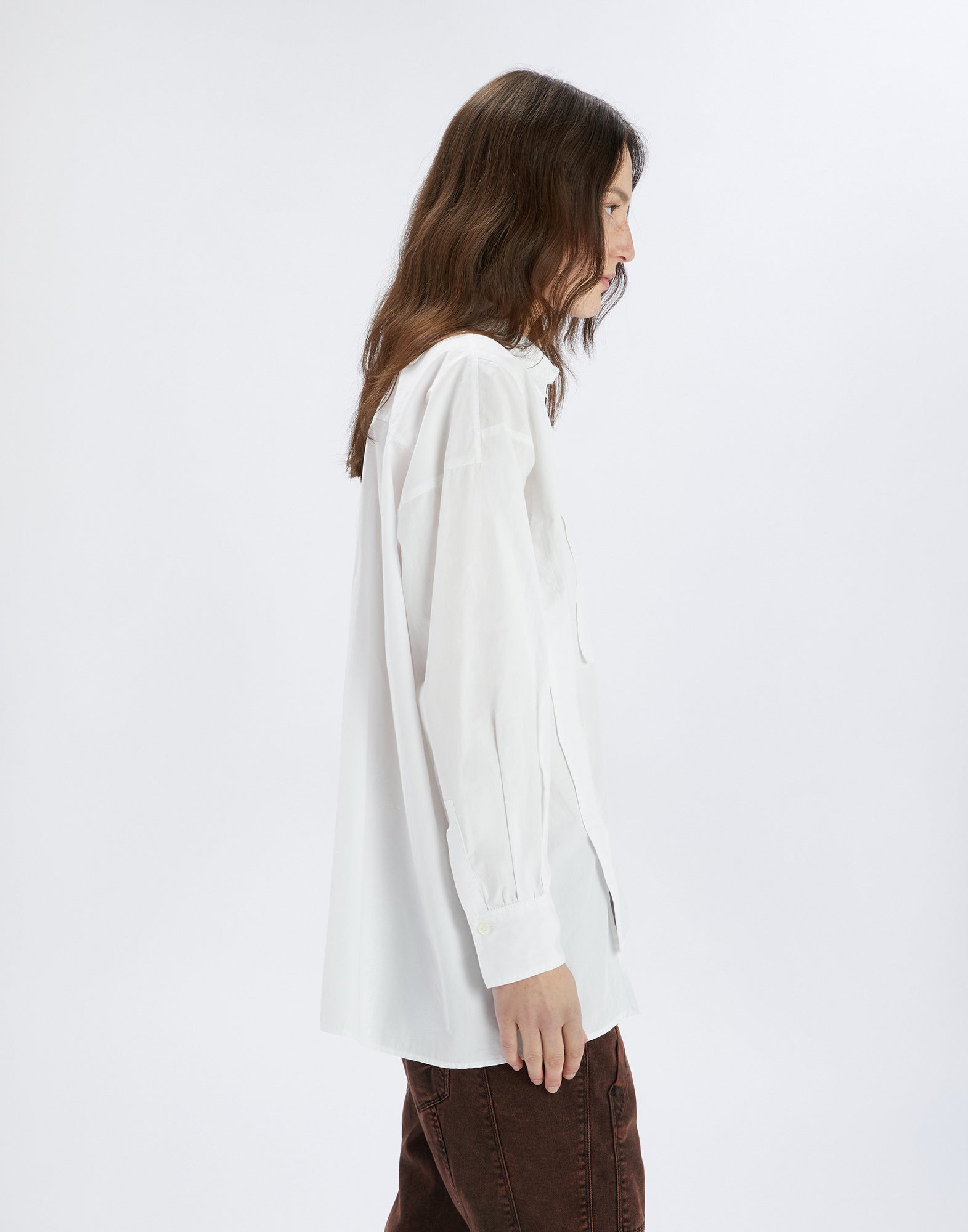 Side view of the DEADLINE shirt, loose-fitting and white with long sleeves, turn-down collar, chest pocket, and dropped armhole, worn by a person.