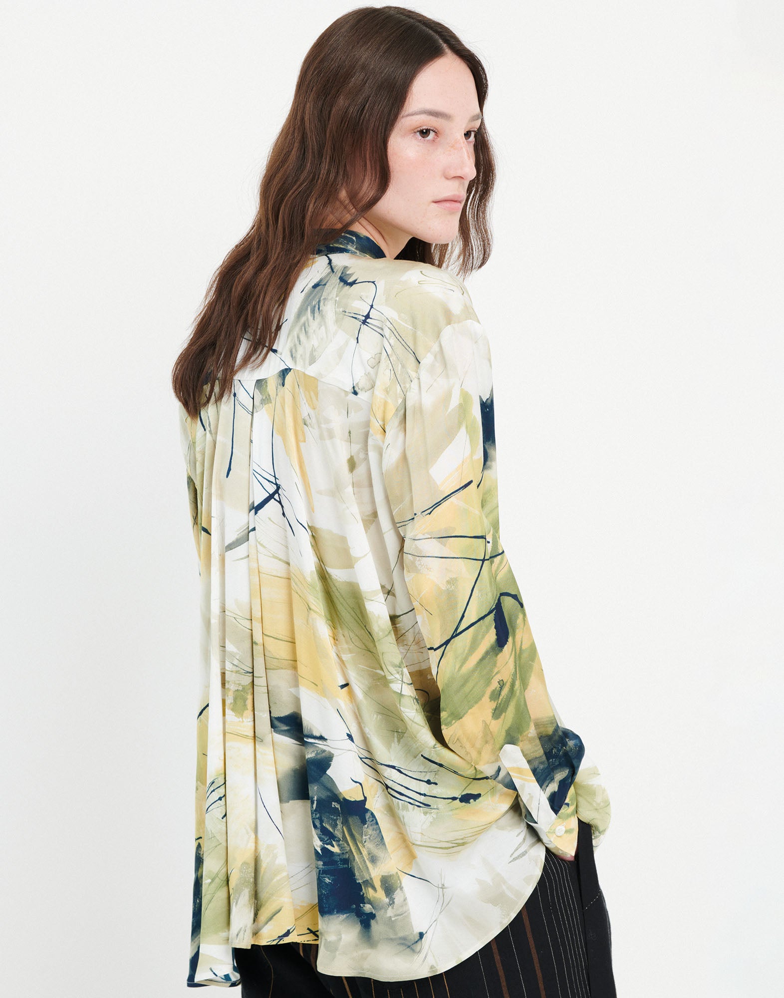 Side view of a person wearing the KINFOLK shirt, airy with abstract print in yellow, green, and cream tones, slight pleating at the back.