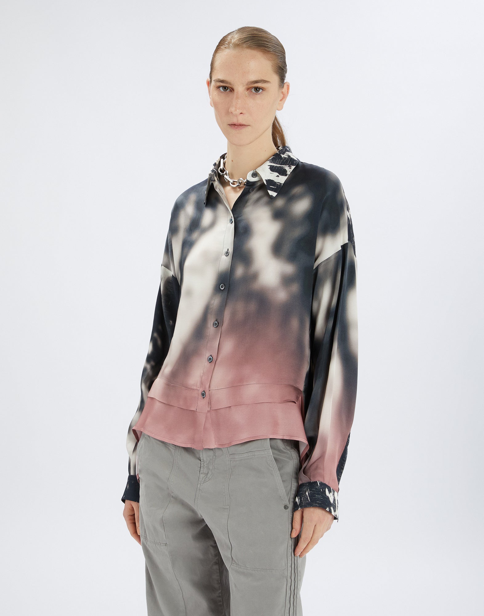 Front view: A woman wears the O-ZONE shirt with creative white-black contrast that smoothly fades into powder pink, relaxed airy fit and turn-down collar.