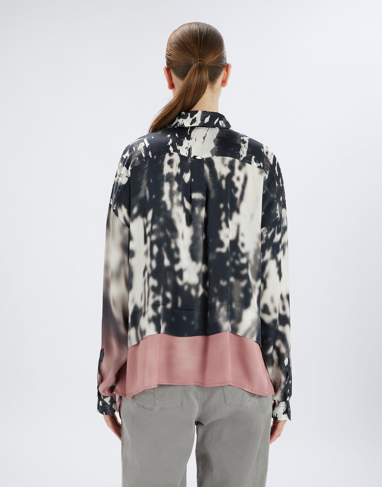 Back view of a person wearing the O-ZONE shirt; creatively patterned in black and white, softly blending into a powder pink area at the lower hem.