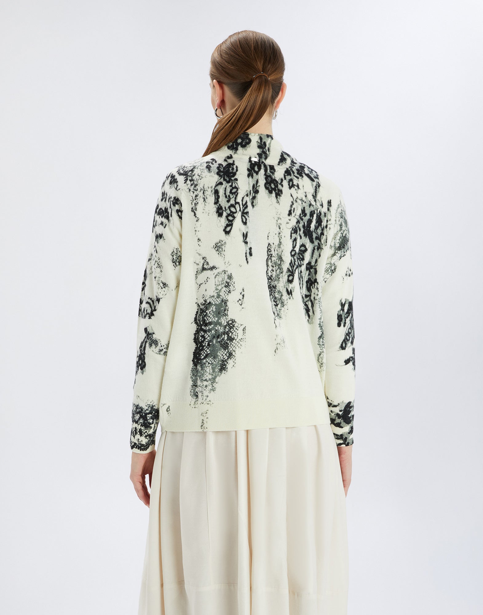 Back view of RAMSEY sweater on cream background with black artistic stripe print, worn by woman with loose hair bun.