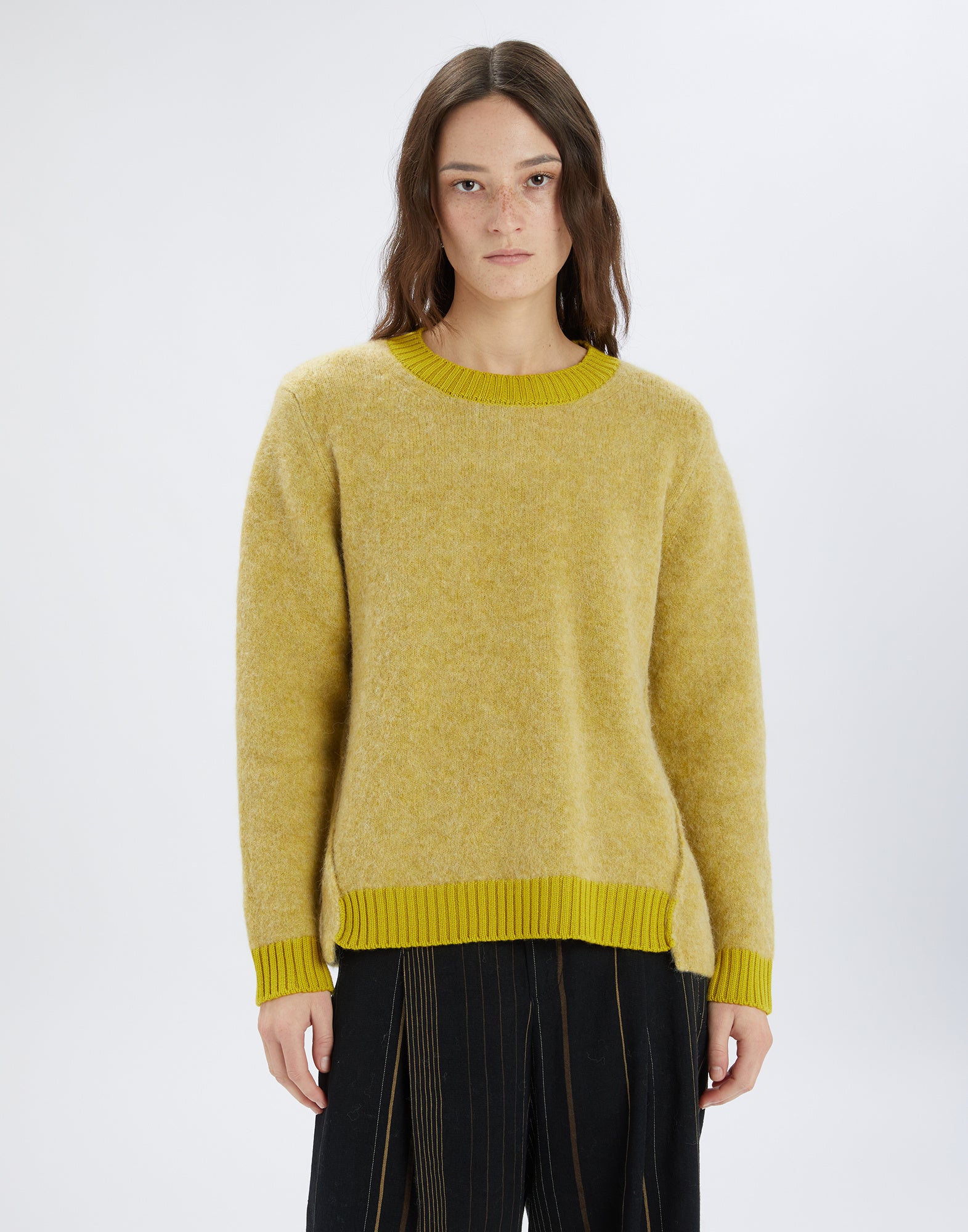 Front view: person wearing the ISADORA sweater, yellowish color with contrasting ribbed trims at collar, sleeves, and hem, relaxed fit.