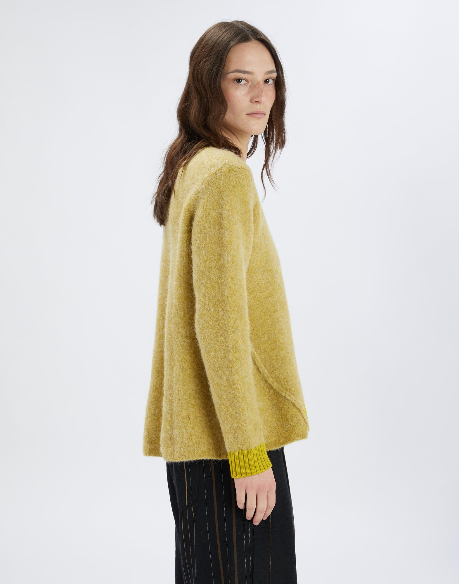 Seitenansicht einer Person, die den Pullover ISADORA trägt; aus gelblichem Woll-Alpaka-Mix mit kontrastierendem Strickbündchen an Ärmel und lockerem Schnitt.