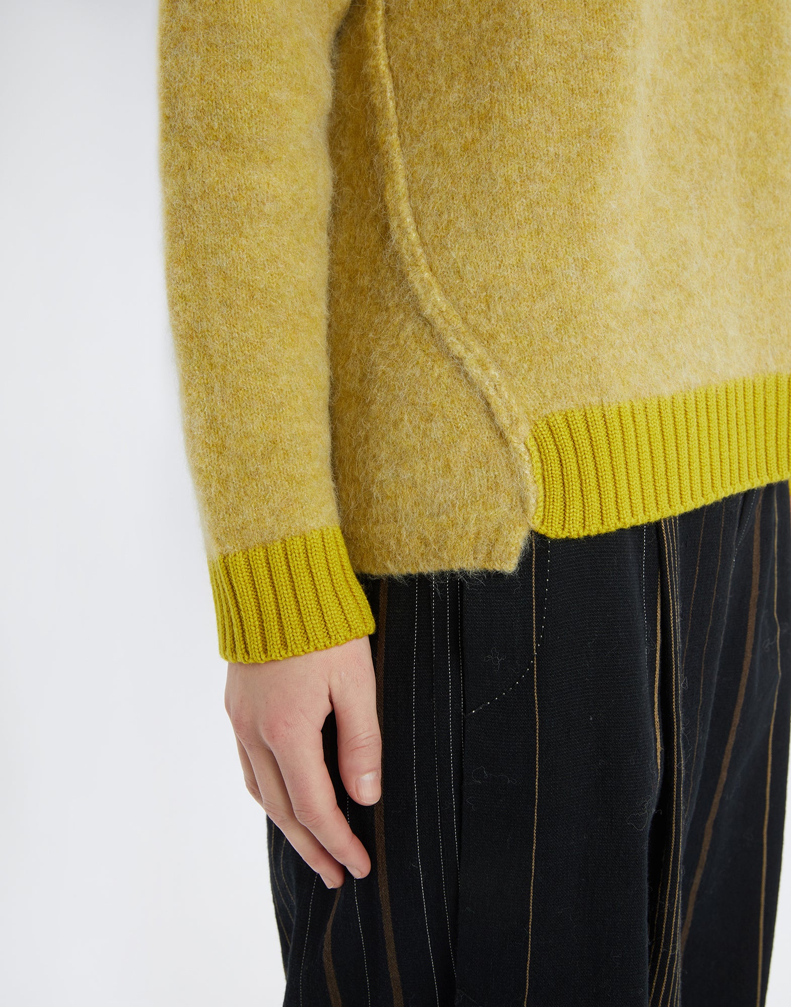 Detailansicht des Pullovers ISADORA, zeigt das gelbe, flauschige Alpaka-Woll-Material mit kontrastierenden Rippenbündchen am Ärmel und Saum, getragen an einer Person.