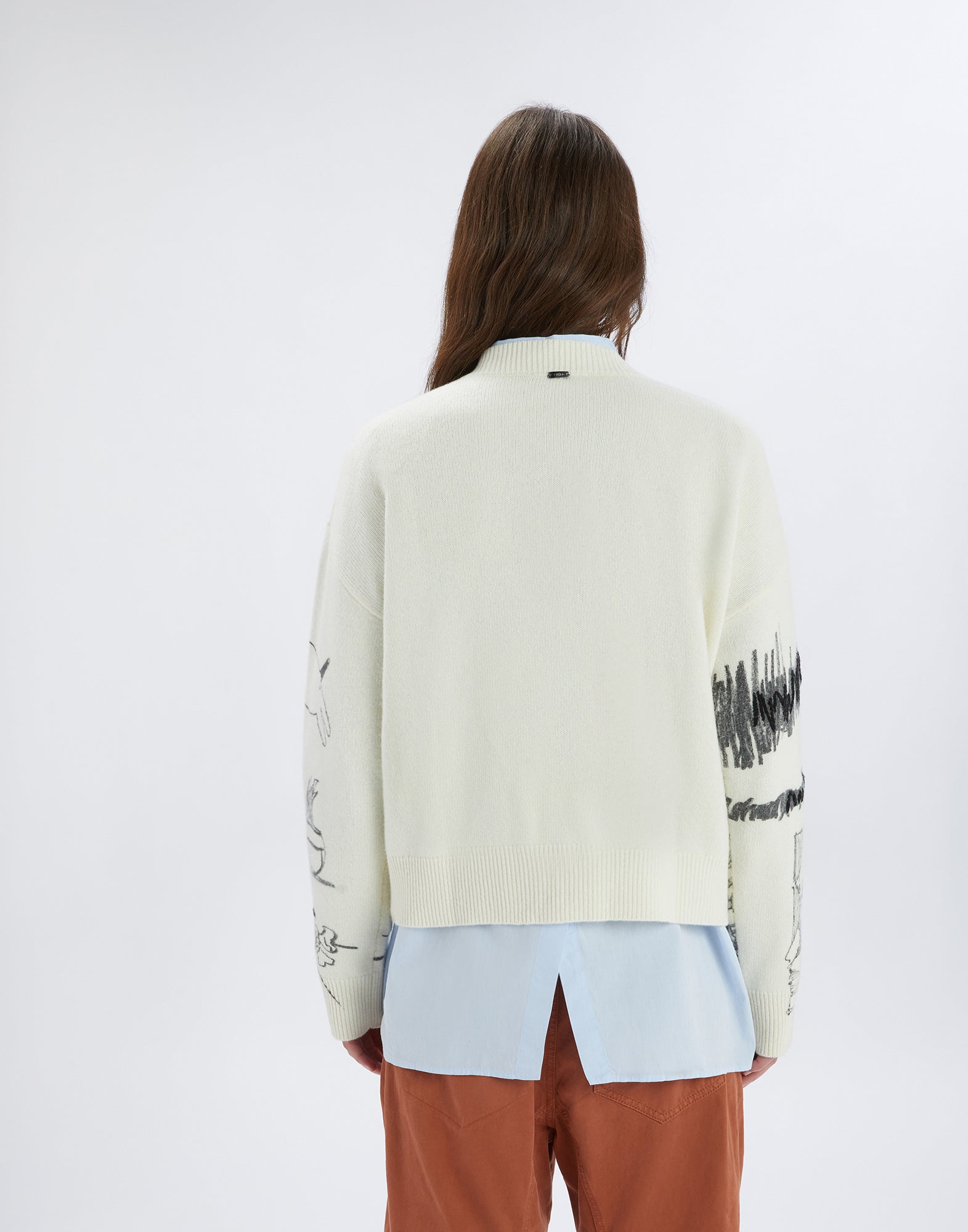 Back view of the APLOMB sweater worn by a person. Cream-colored wool sweater with boxy fit and embroidered black designs on the sleeves.