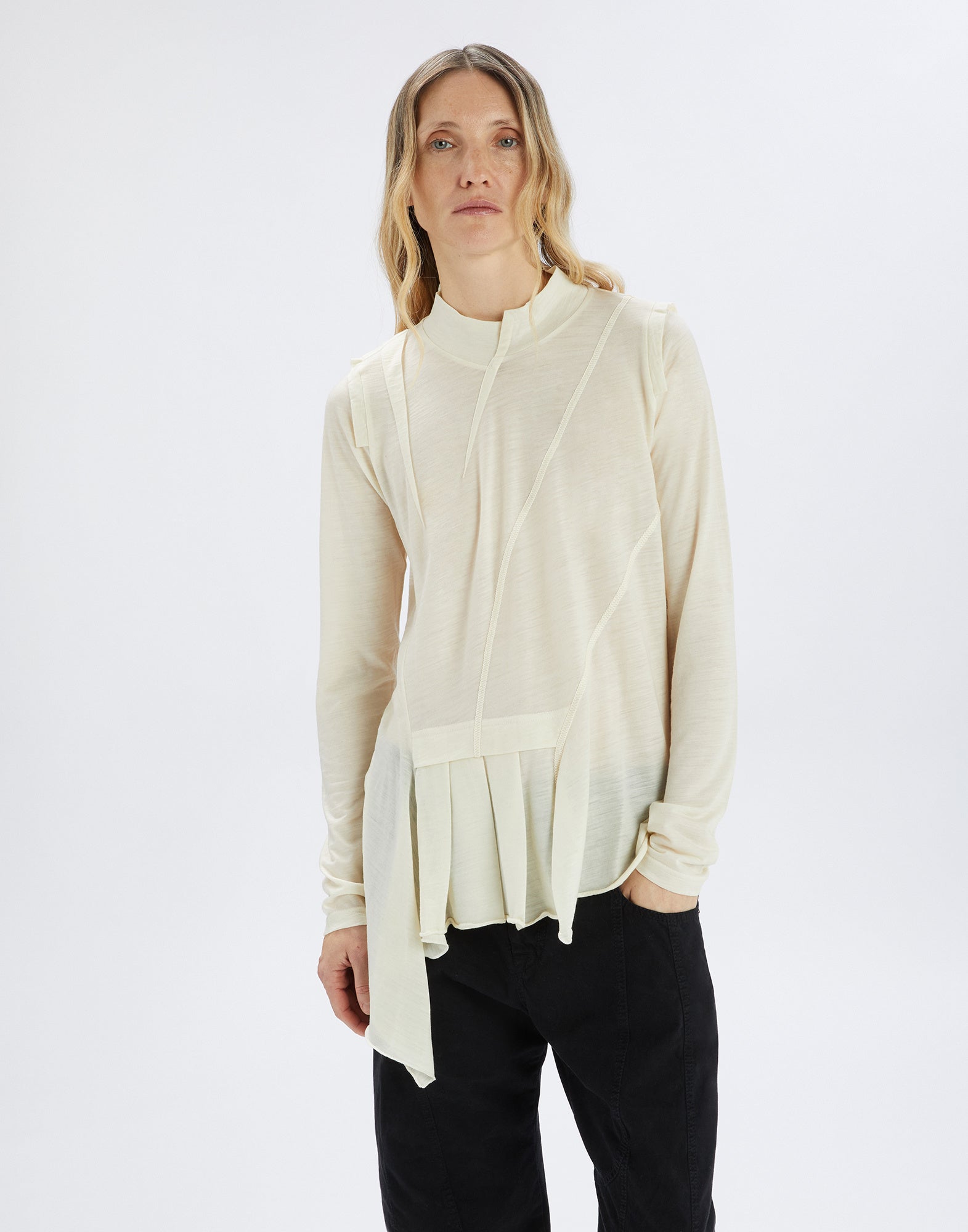 Front view of the MATELOT, an ultra-lightweight wool jersey sweater in cream with stand collar, asymmetric cut, long sleeves, and irregular hem, worn by a person.