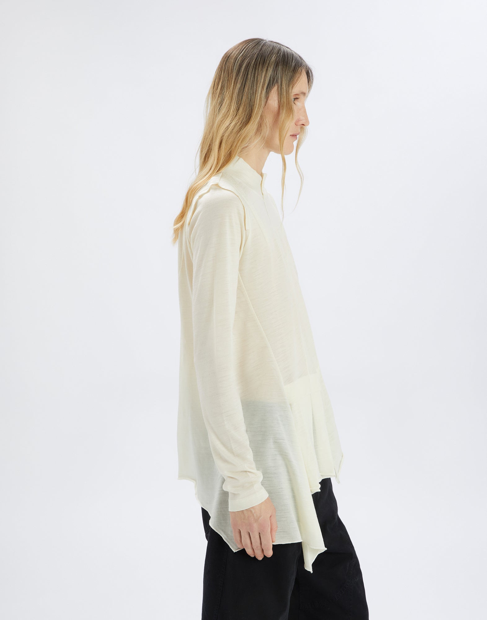 Seitenansicht eines Models, das den Pulli MATELOT trägt. Helles, ultraleichtes Woll-Jersey mit Stehkragen, langen Ärmeln und asymmetrischem, unregelmäßigem Saum.