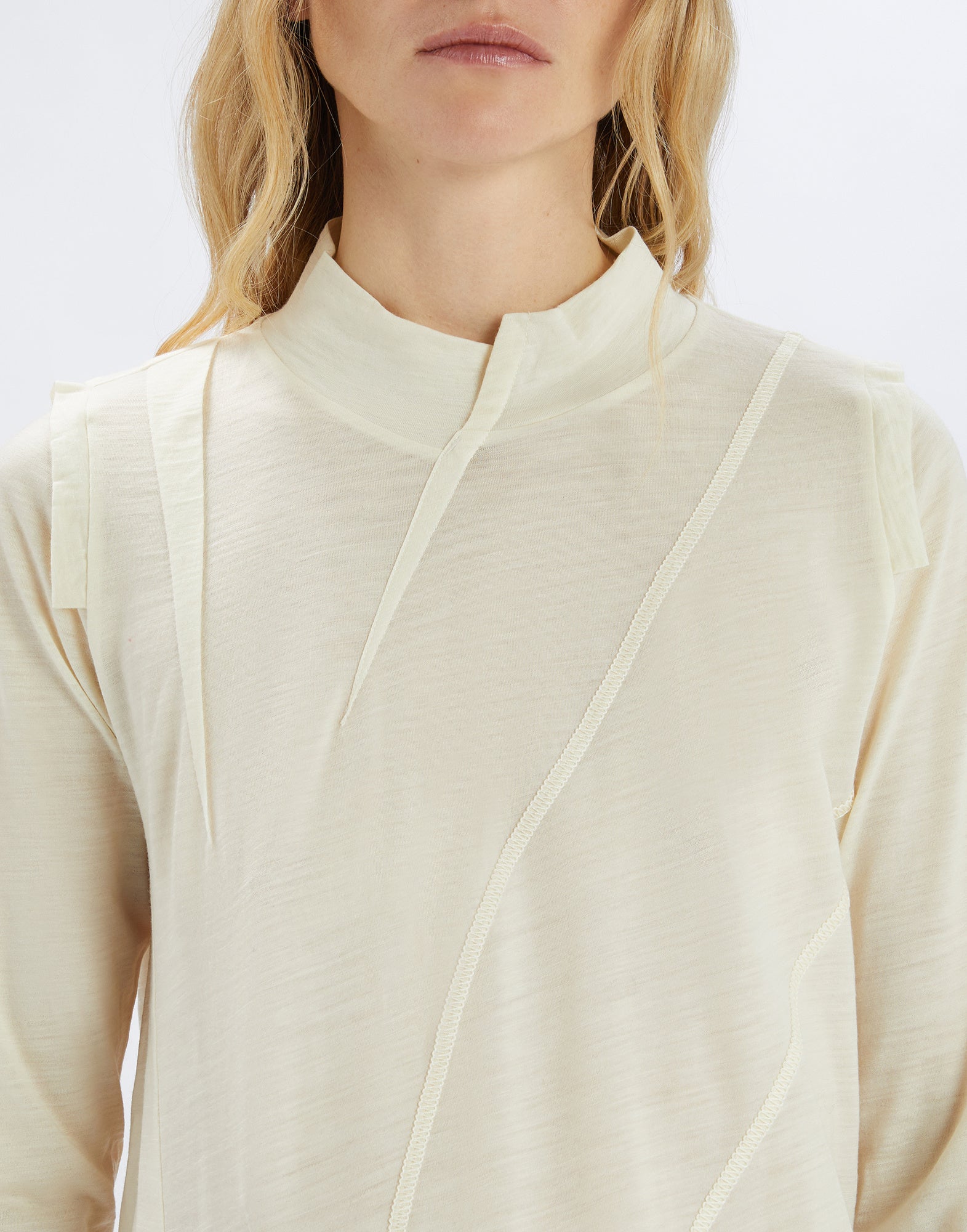 Frontalansicht vom Oberkörper einer Person, die den cremefarbenen MATELOT Pullover mit Stehkragen, asymmetrischen Schnitten und unregelmäßigem Stoffband trägt.