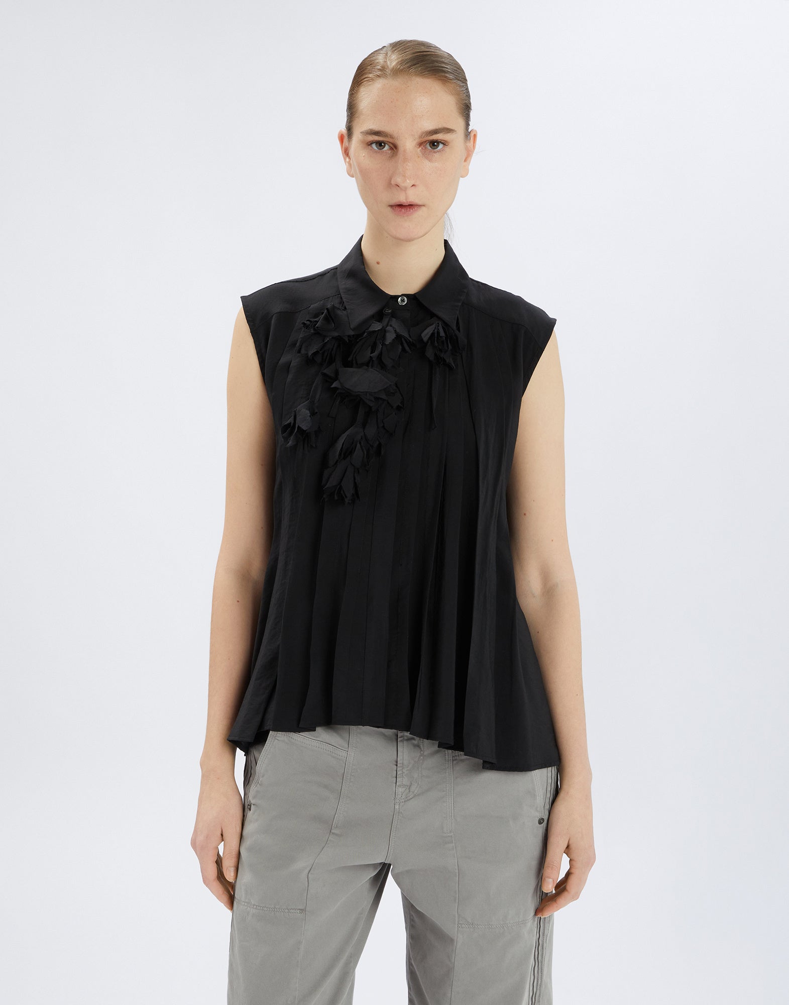 Front view: DOODLE sleeveless black shirt with turn-down collar, pleated seams, and striking tone-on-tone floral applique at the collar.