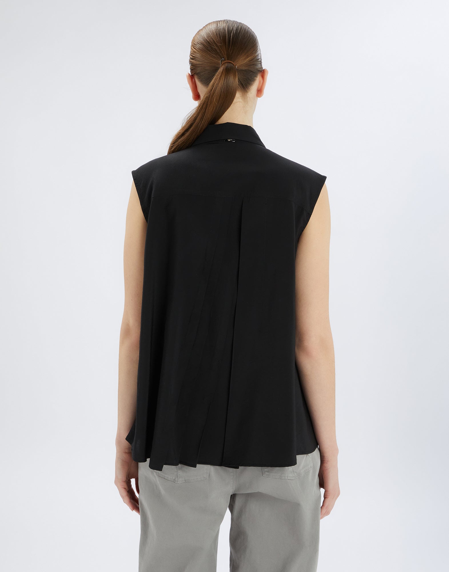 Back view of the sleeveless DOODLE blouse in black with rounded back hem, irregular pleats, and lightweight, flowing fabric.