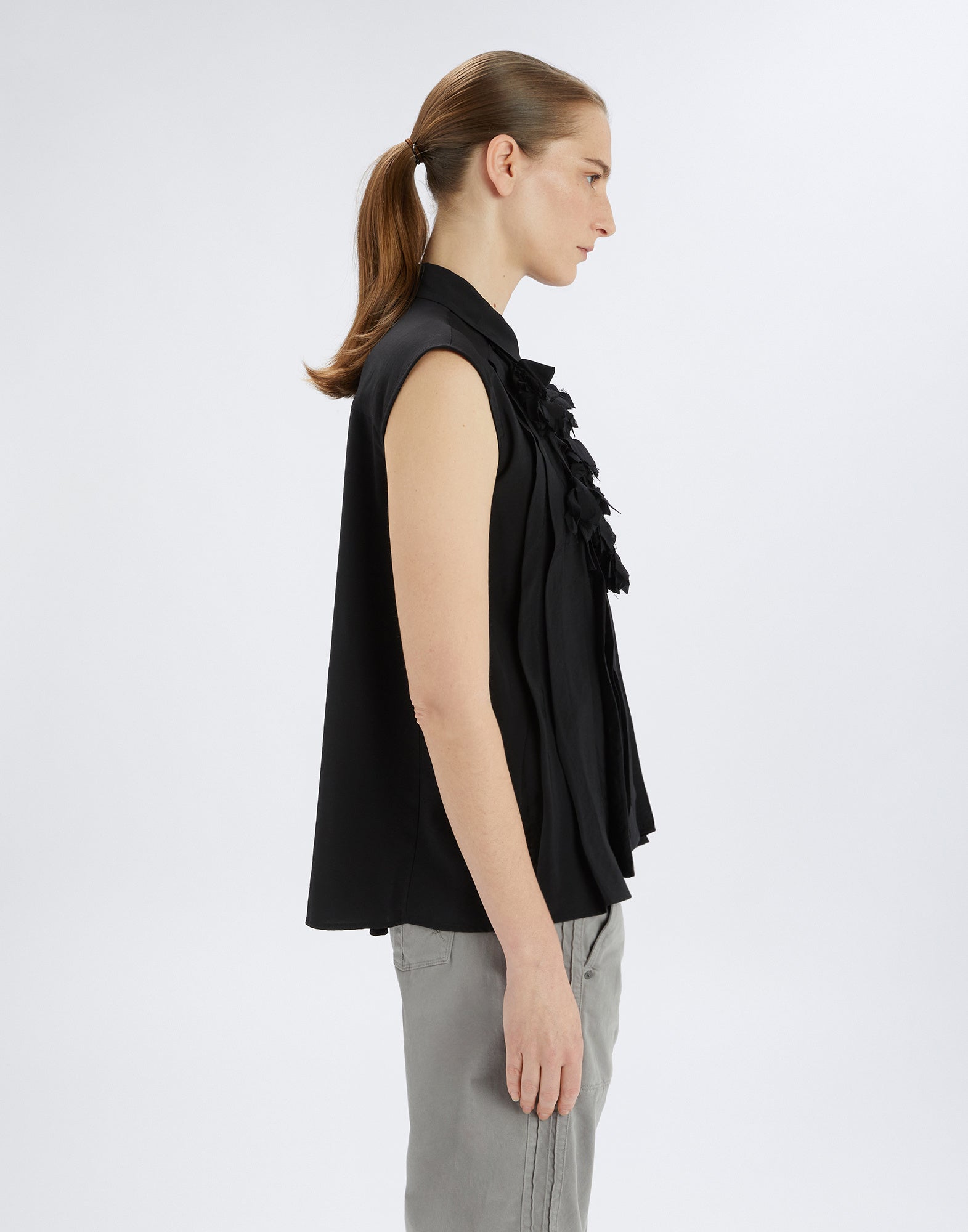 Side view of model wearing the sleeveless black DOODLE blouse with tone-on-tone floral applique detail, irregular pleats, and rounded hem.