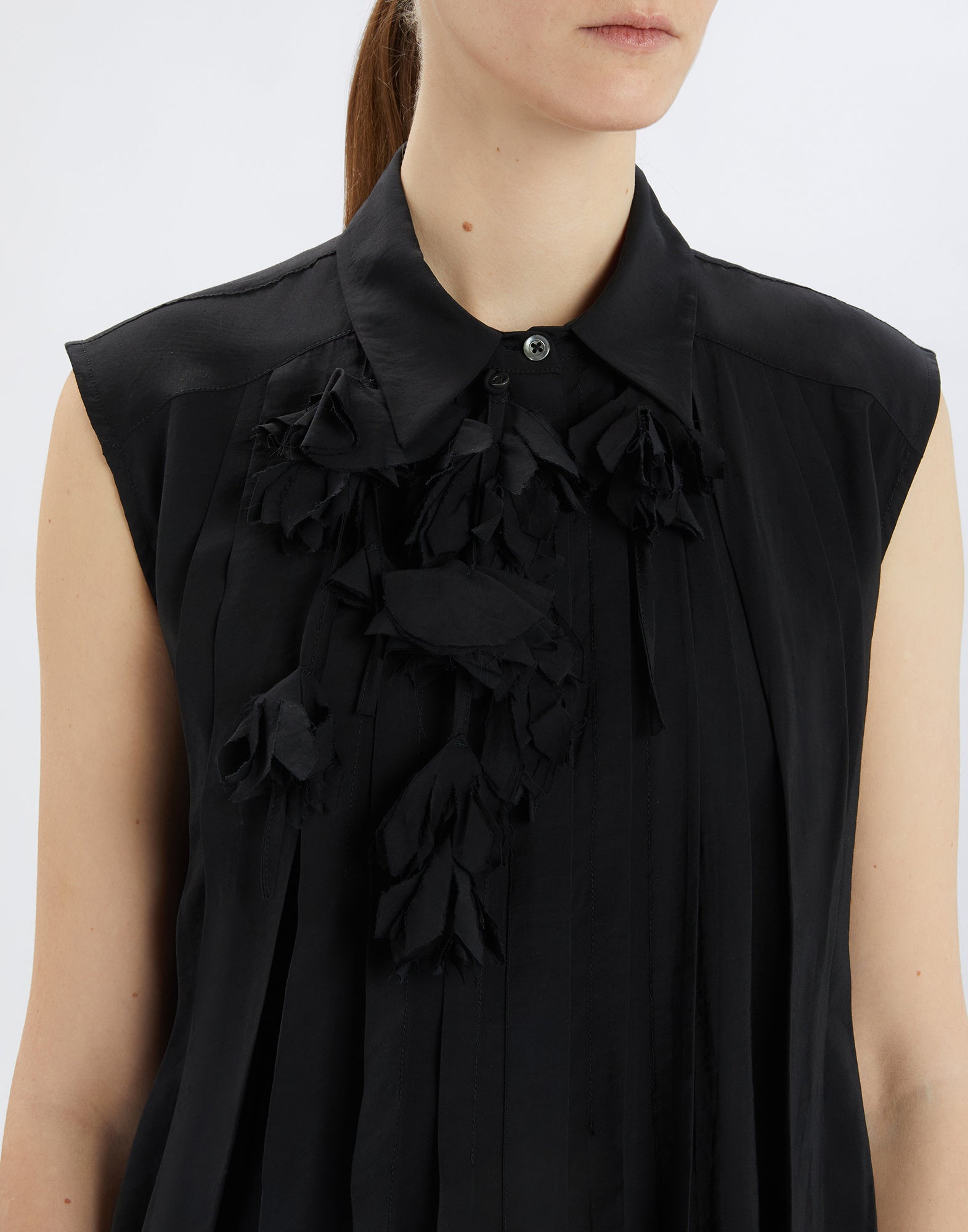 Front view of the DOODLE blouse, sleeveless black model with turn-down collar, removable tone-on-tone floral applique, stitched pleats and lightly crinkled effect.