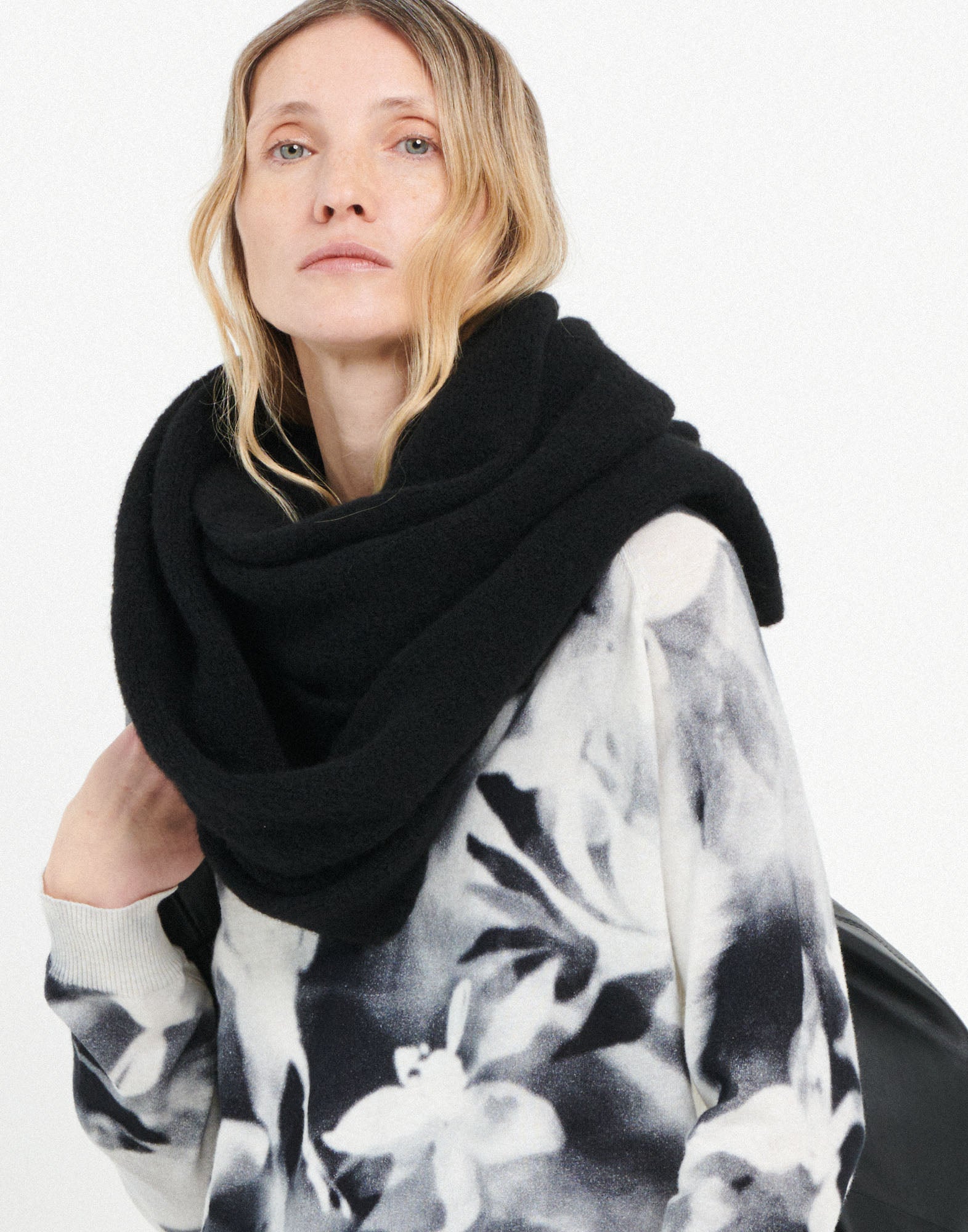 Front view: A person wears the FROSTY stretch alpaca wool scarf in black loosely around the neck. The material appears soft and voluminous.