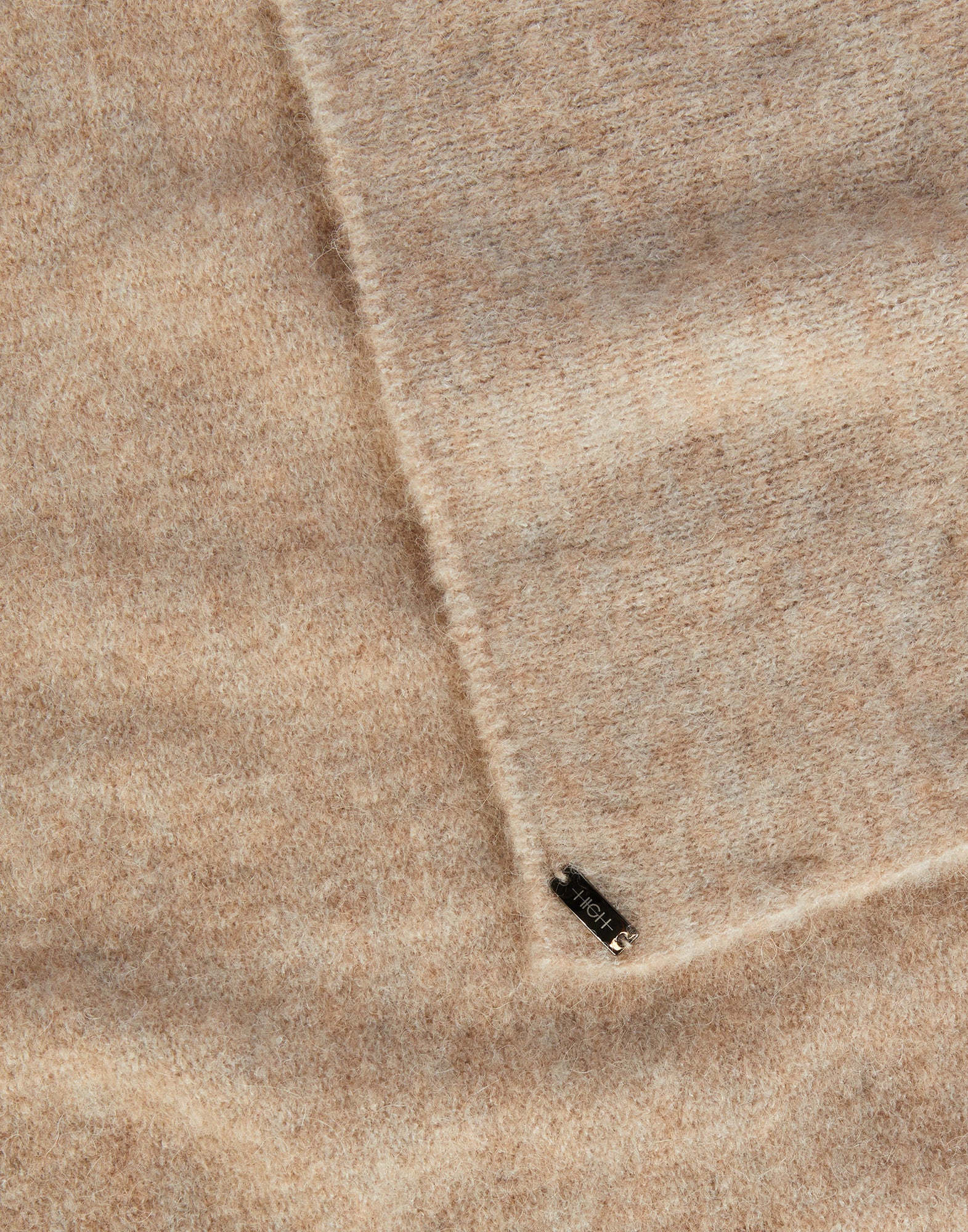 Close-up view of FROSTY, an airy stretch alpaca wool scarf in beige with a soft texture, showing the material and a small metal label inscribed 'HIGH'.