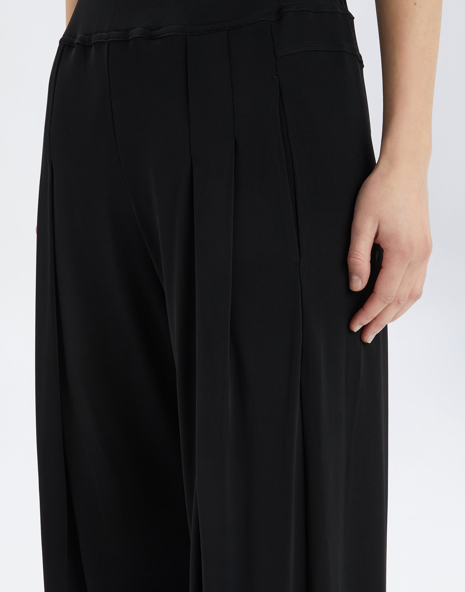 Detailansicht der SLIP-OVER Hose aus schwarzem Viskosejersey, mit weichen Falten an der Vorderseite und seitlicher Eingrifftasche, aus Nähe betrachtet.