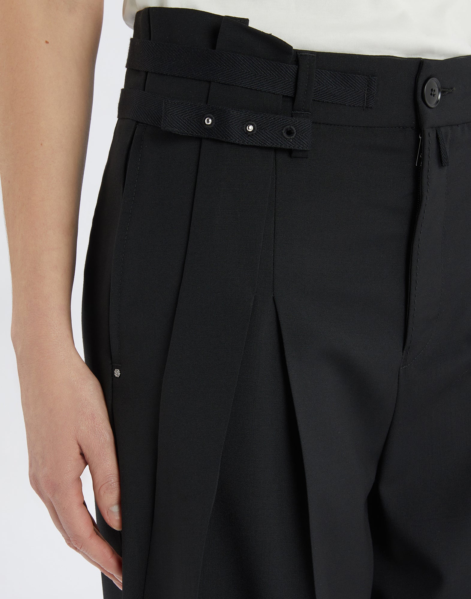 Detailed view of NEVERLAND pants in extra-fine wool, showing double front pleats, belt with rivets, and button closure from a frontal perspective.