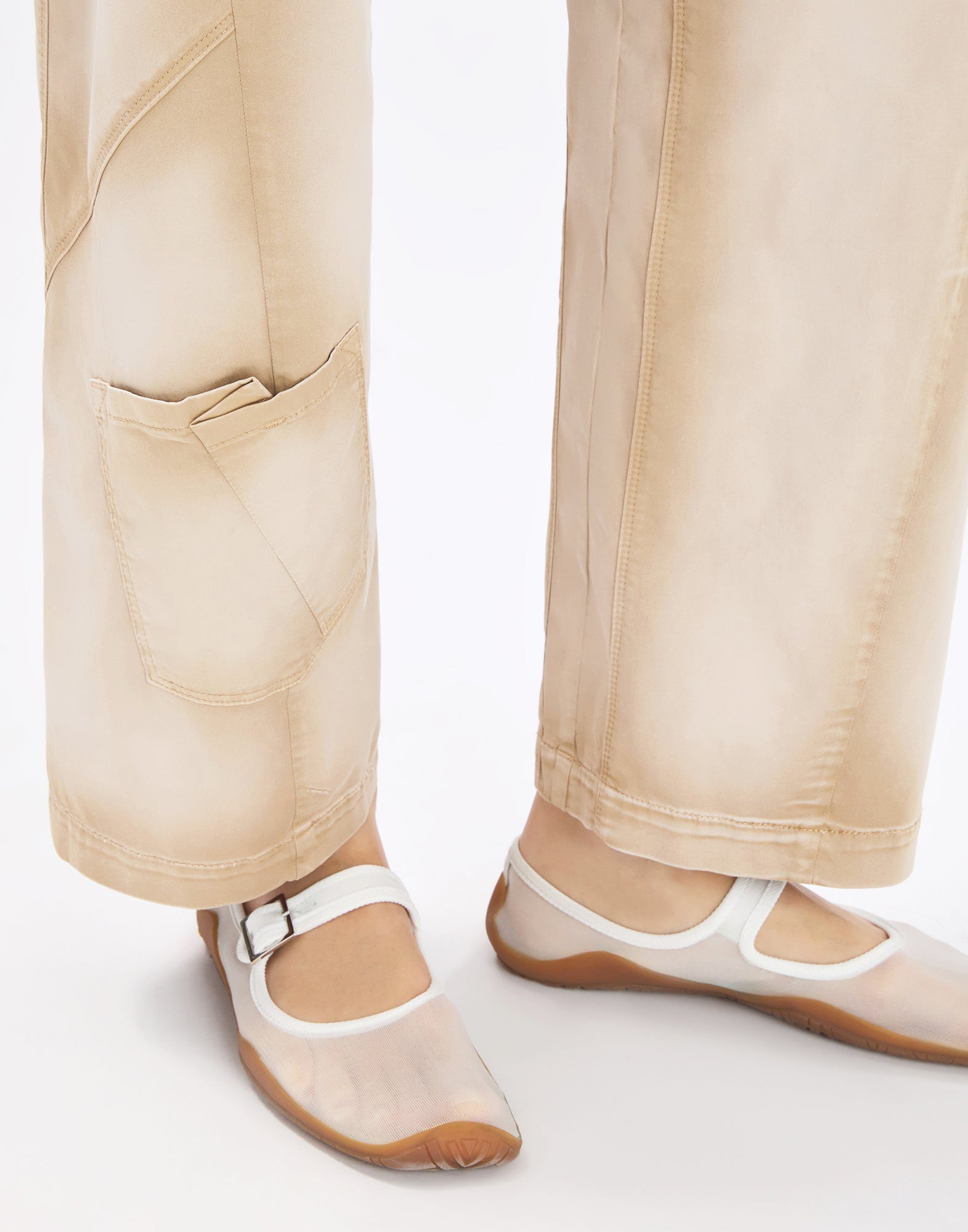 Detailansicht: OUT-SHINE Hose in hellem Beige, ausgestelltes Bein mit ausgeprägten Nähten und aufgesetzter Beintasche, getragen mit transparenten Mary-Jane-Schuhen auf neutralem Hintergrund.