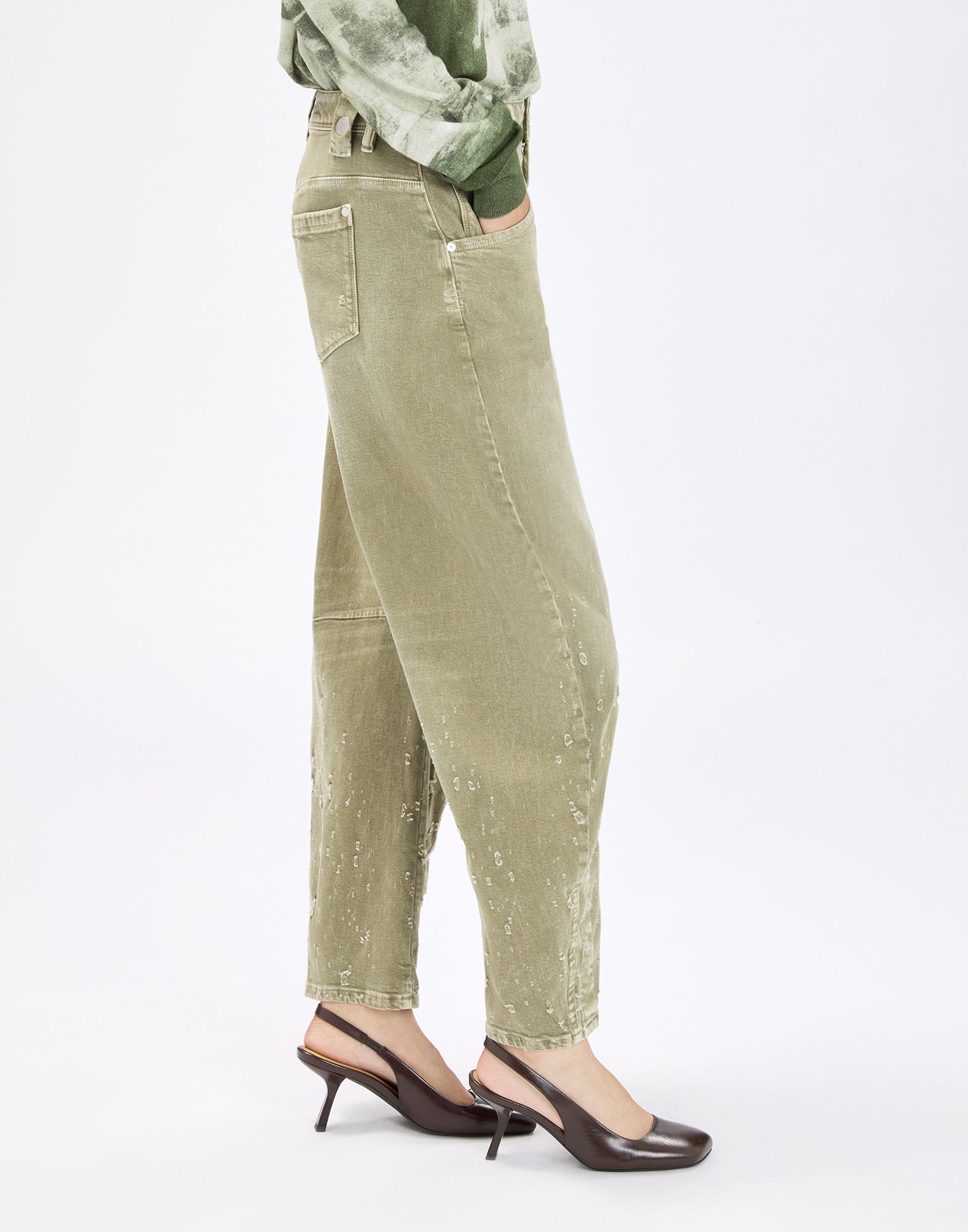 Side view: person wearing the loose-fit, olive green vintage HAPPILY pants with exposed seams, subtle worn-in details and a patch back pocket, paired with heeled slingback pumps.