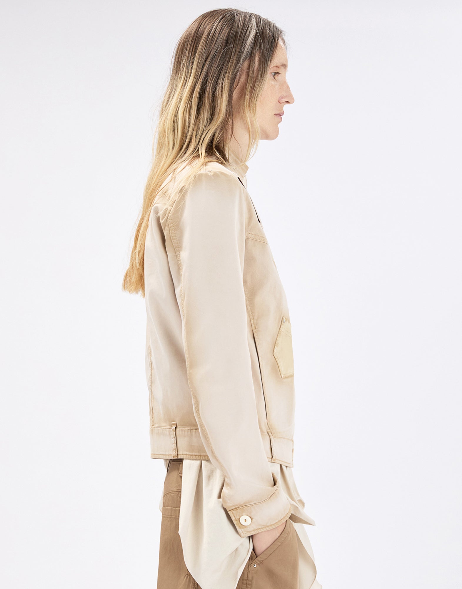 Side view: person wearing the beige ONSET cotton-satin jacket with subtle ombre effect, chest patch pocket and buttoned cuffs, paired with light brown trousers against a neutral background.