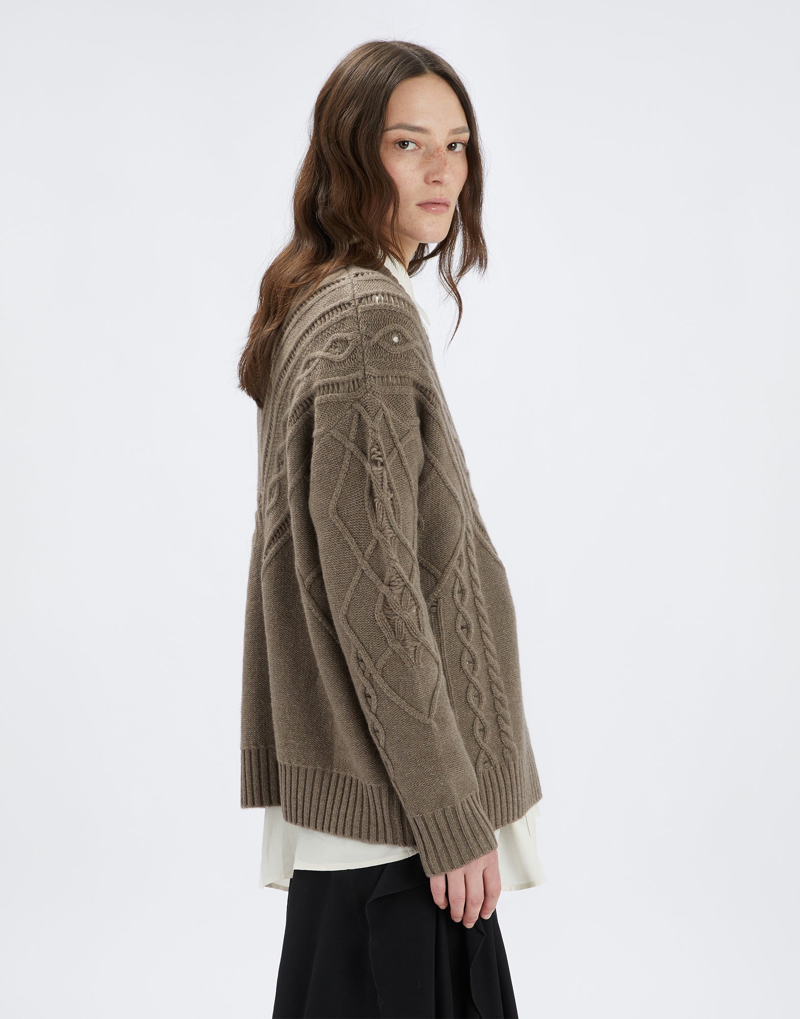 Seitenansicht des Pullovers NORTON an einem Model, zeigt breite Rippen, diagonale Ajourmuster und geschwungene Zopfmuster sowie gerippte Bündchen und Saum.