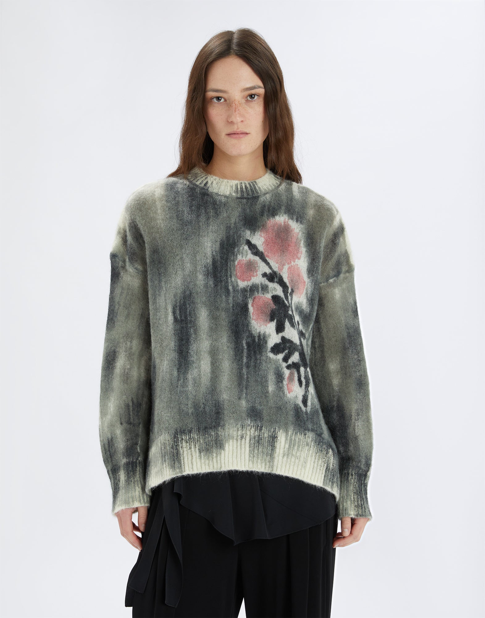 Frontalansicht eines Pullovers namens NEUTRON mit boxy Schnitt, harmonischem Farbverlauf und rosa Blumenmotiv auf der linken Seite. Das Modell trägt den Pullover über schwarzer Kleidung.