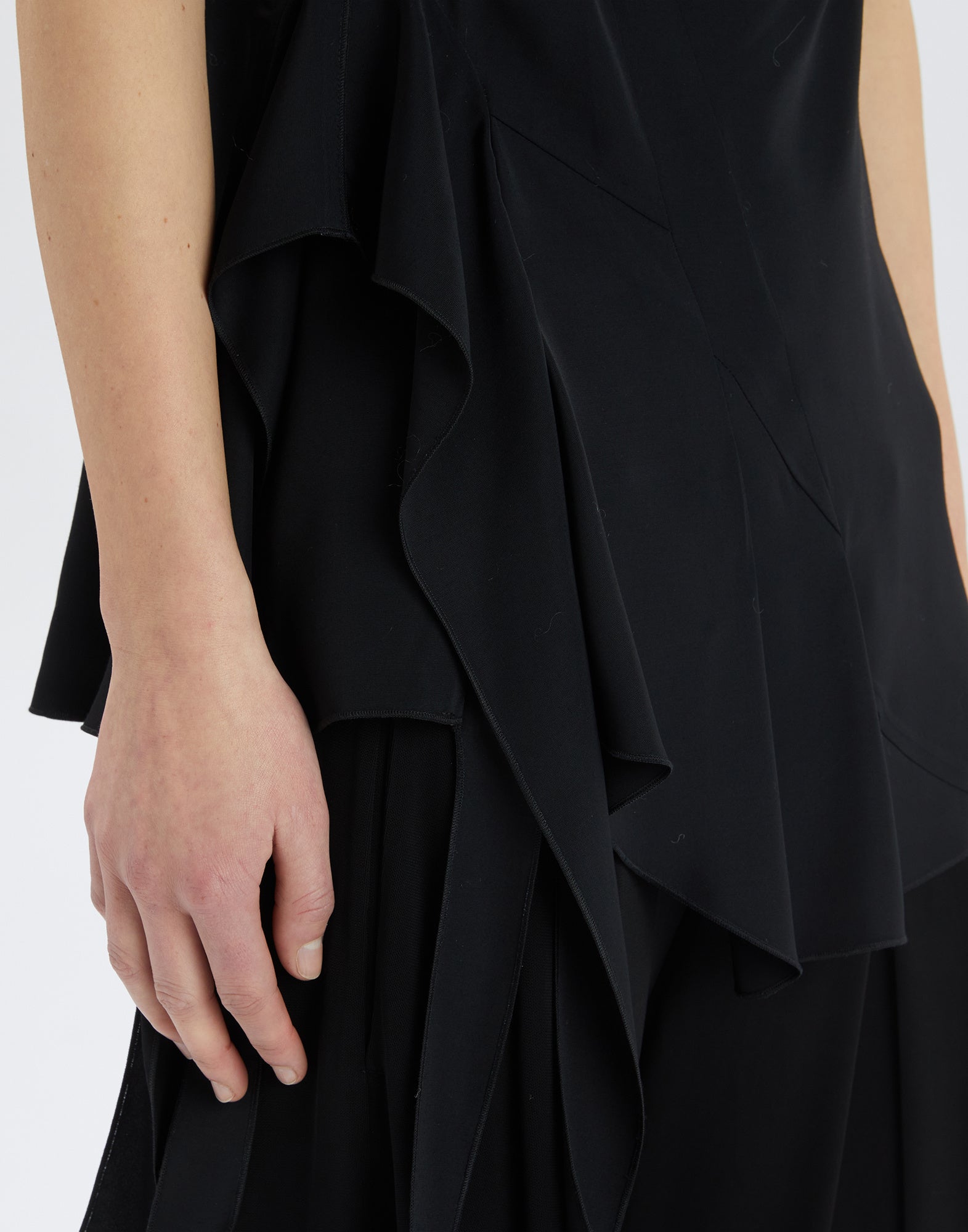 Close-up of the TIMBRELL top, focusing on the side ruffle made of lightweight, flowing black fabric that adds movement and elegance.