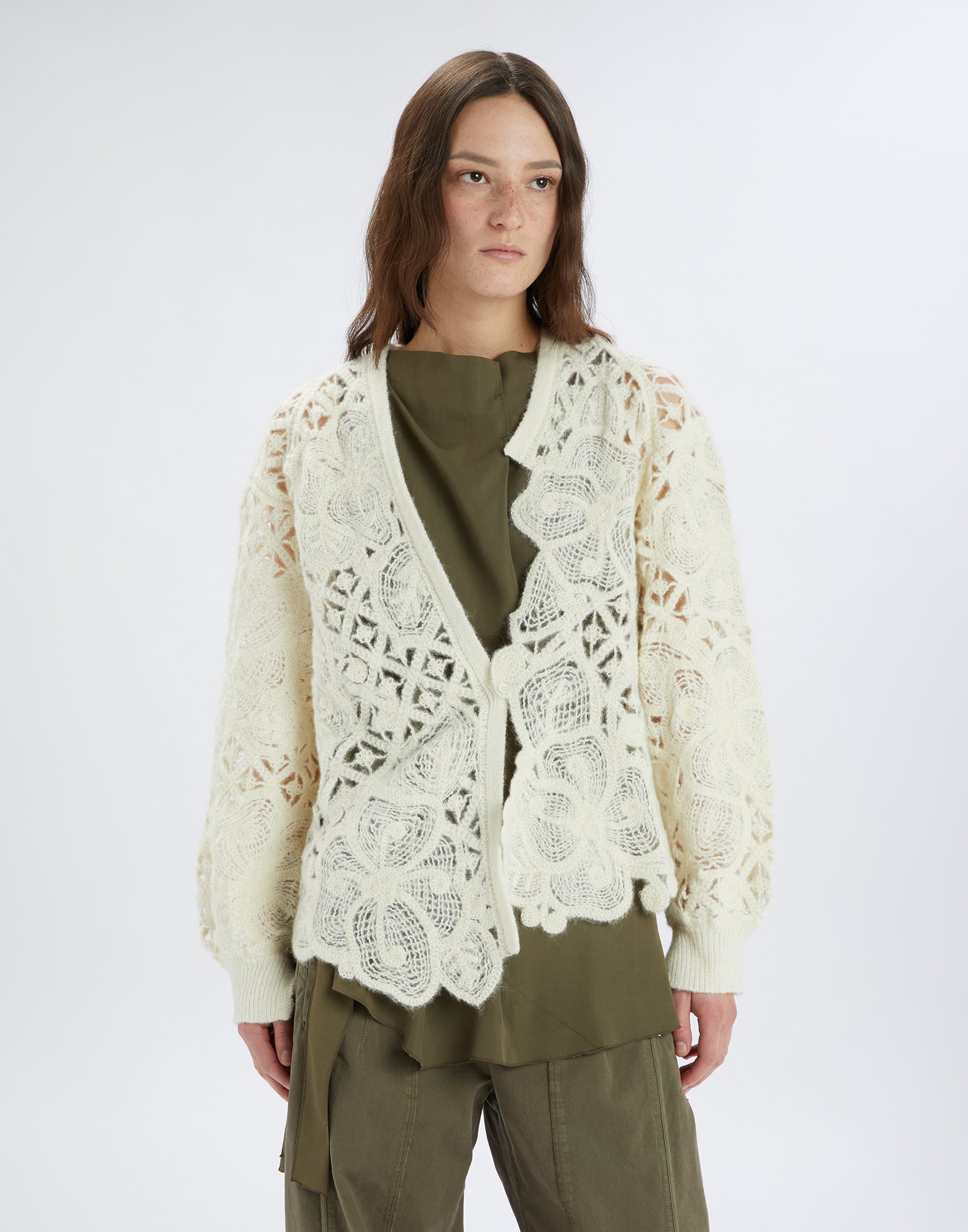 Frontalansicht: BOHEME Cardigan mit cremefarbener, floraler Ajourstickerei, V-Ausschnitt und asymmetrischem Saum, getragen von Frau über olivgrünem Outfit.
