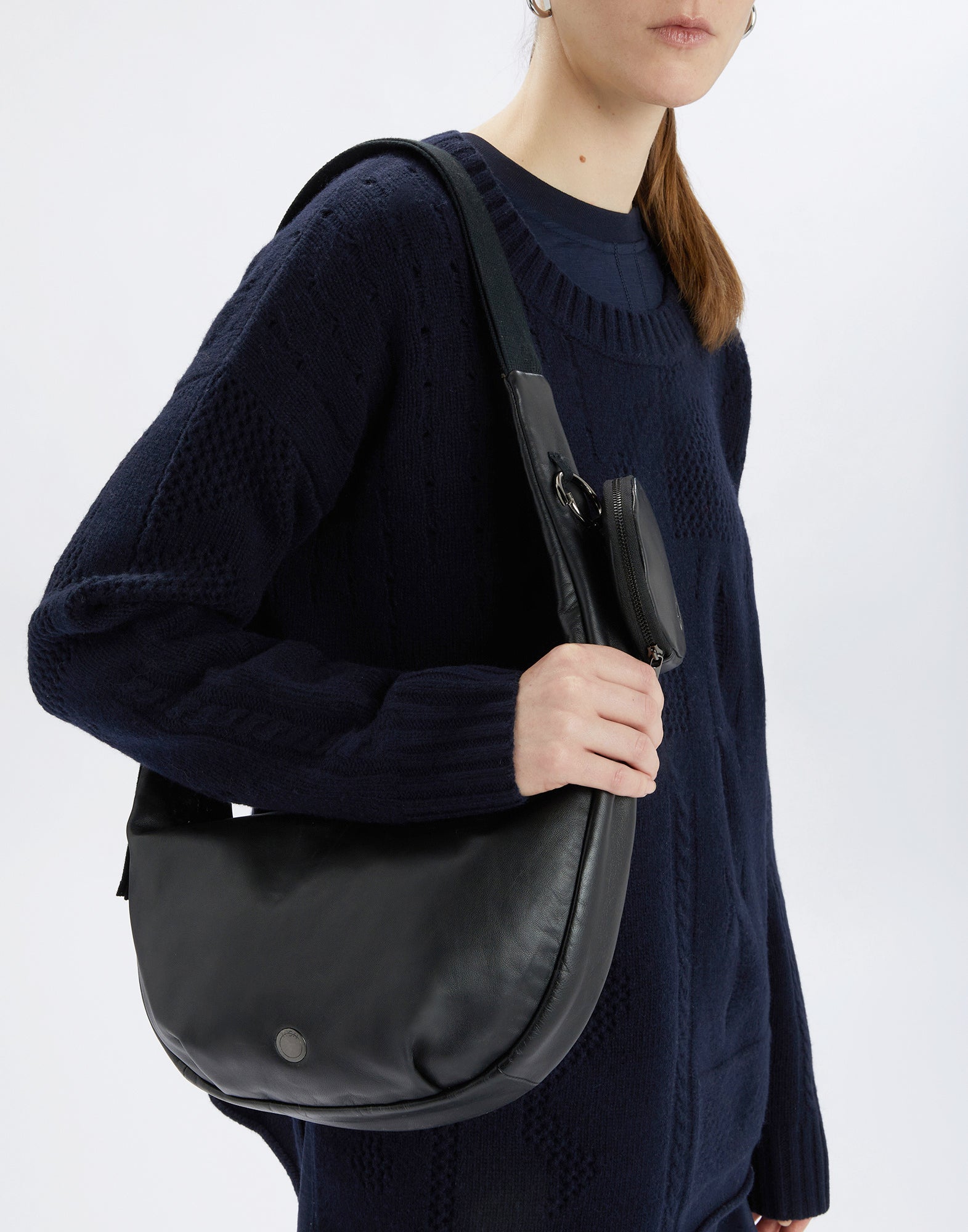 Frontal view of a person wearing the ADMIRAL crossbody bag on the shoulder; black bag with removable round wallet and logo-embossed detail at the bottom.