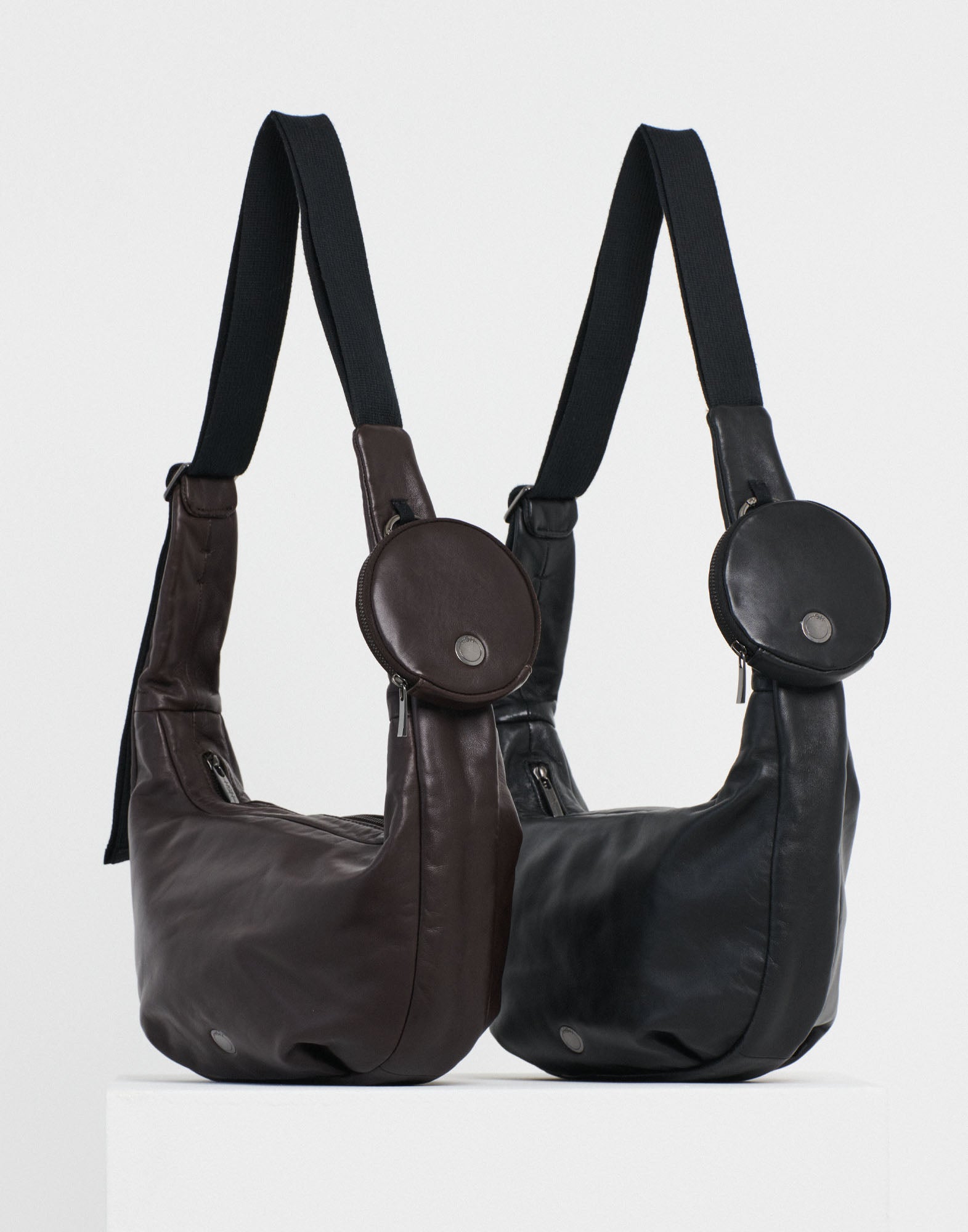 Front view of two ADMIRAL crossbody bags in lamb leather, one in dark brown, one in black, featuring a removable round wallet and a black adjustable shoulder strap.