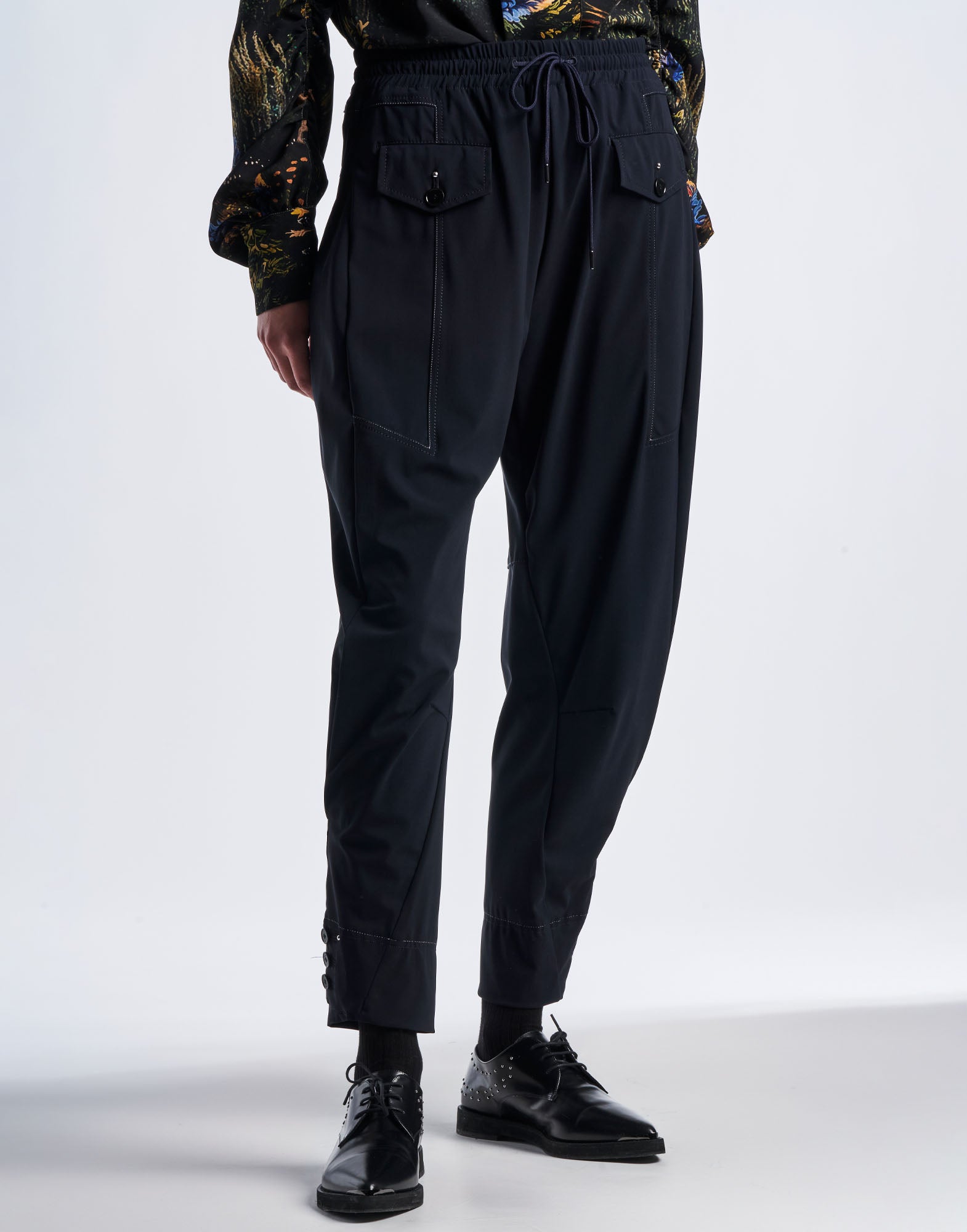Front view of JAUNTY jogger pants with tapered fit, drawstring waist, horizontal pockets with buttoned flap, and visible decorative stitching in sporty Sensitive(R) material.