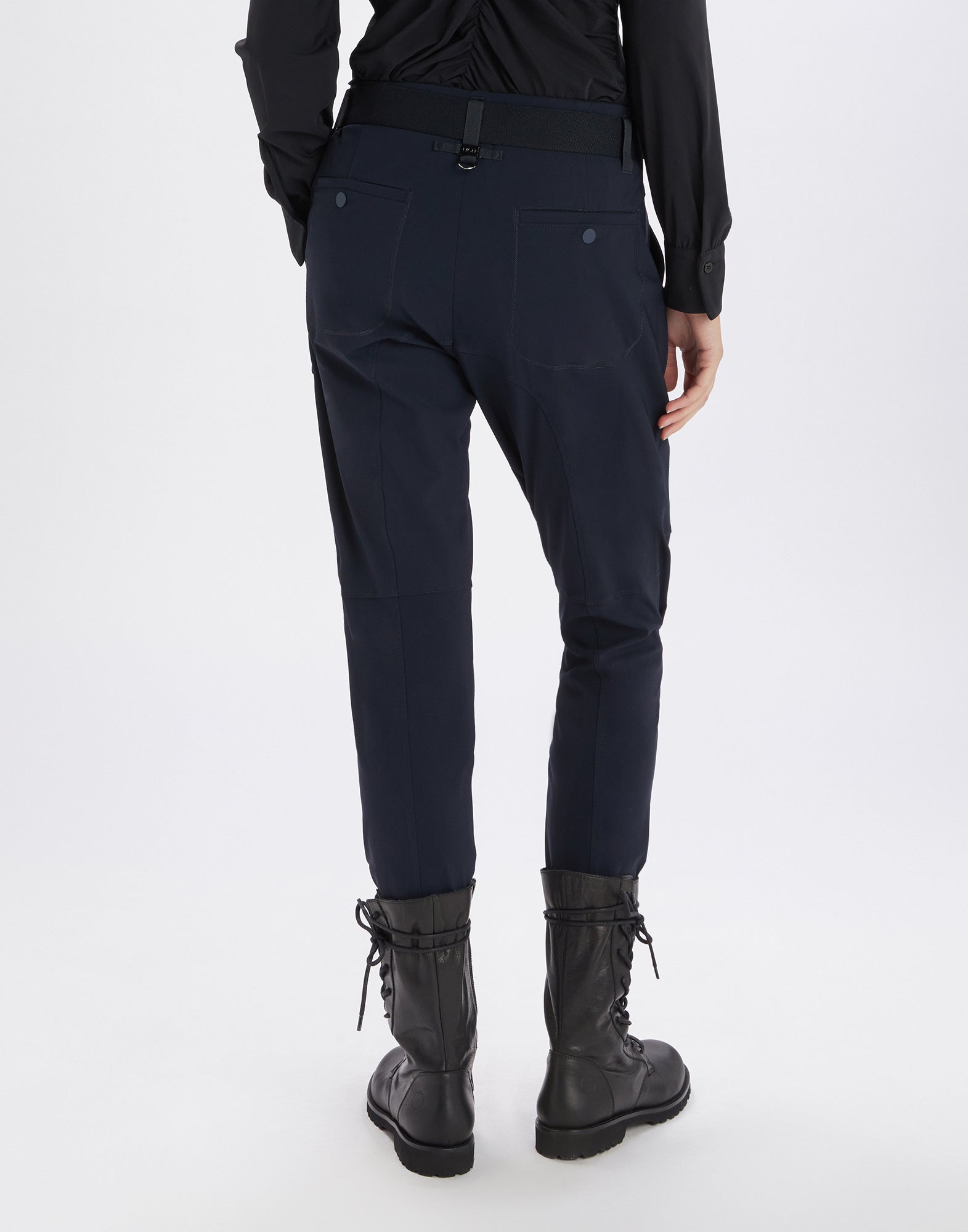 Rückansicht einer Person, die die LURCH Jodhpur-Hose in Dunkelblau trägt; elastischer Bund mit Gürtel und Paspeltaschen, kombiniert mit schwarzen Stiefeln.