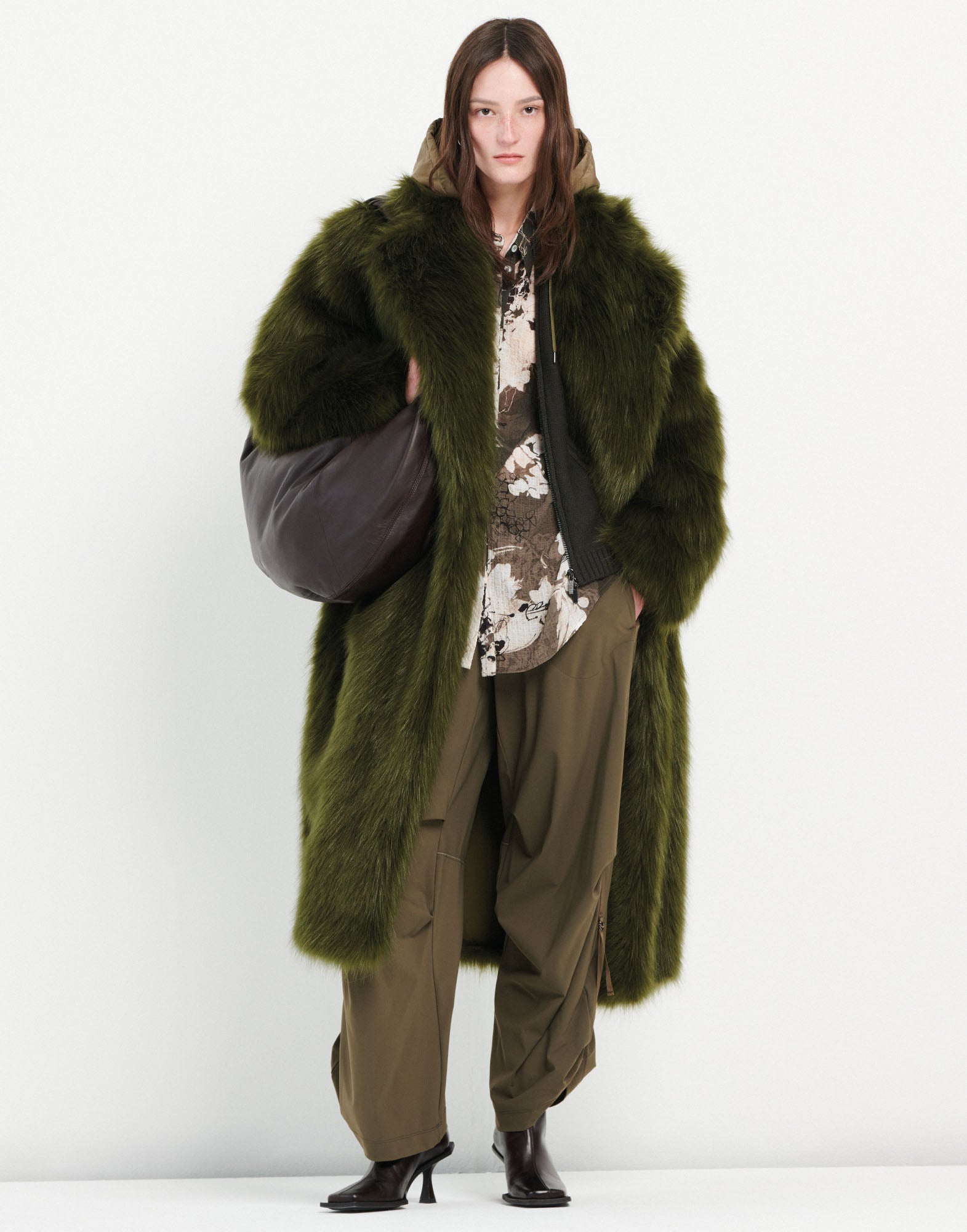 Front view: Model wears the OUTGOING trousers with wide legs, drawstring waist, and D-ring detail at the hem, paired with long green coat.