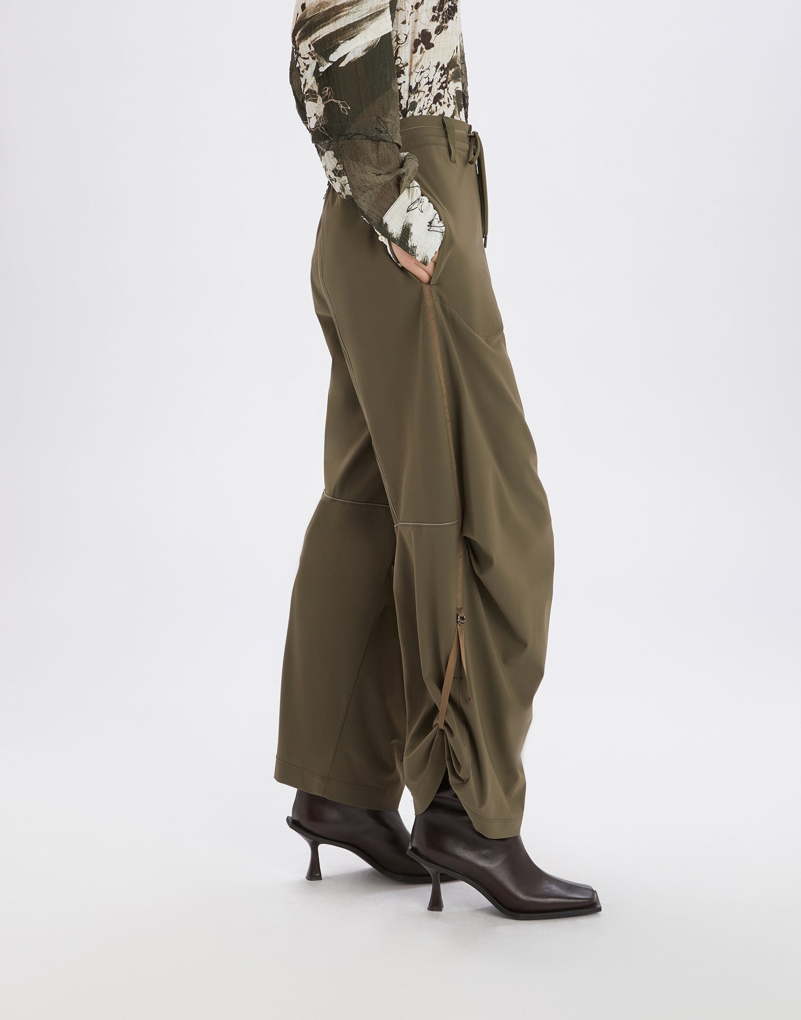 Side view of OUTGOING trousers in olive green featuring wide leg, drawstring waist, distinctive side pockets, and adjustable hem with D-ring.