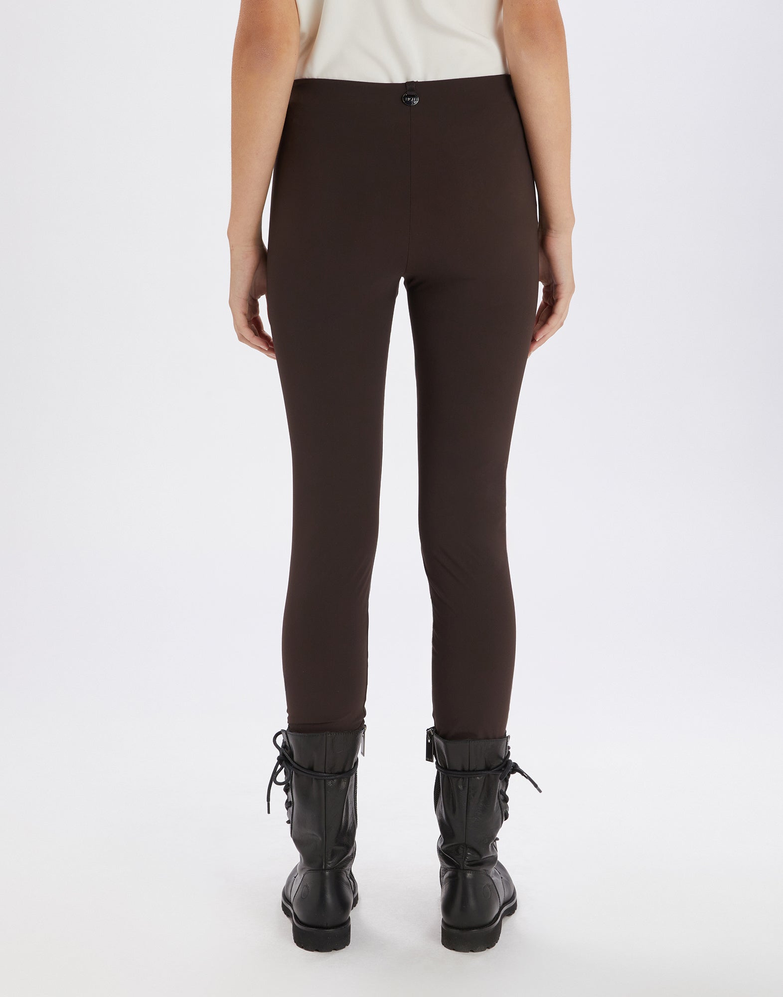 Rear view of a person wearing JEEPERS leggings in brown Sensitive(R) material with no seams or pockets, paired with black boots.