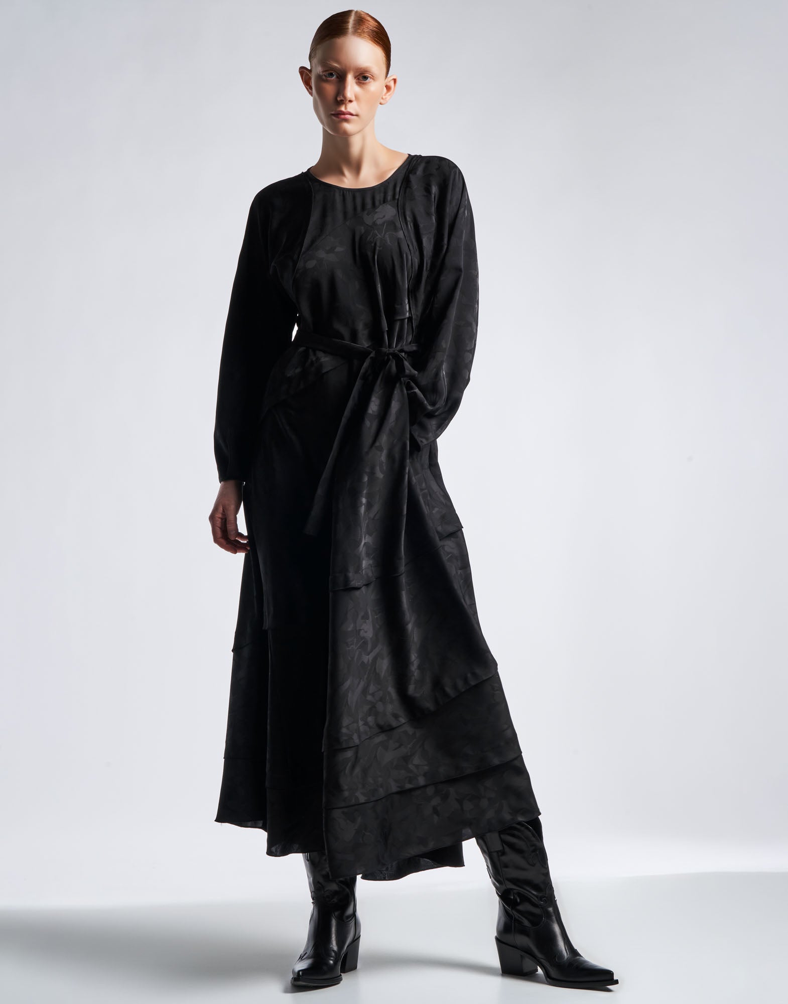 Front view: A woman wears the FAVOURITE maxi dress in black technical satin floral damask, round neckline, waist tie, and flared skirt.