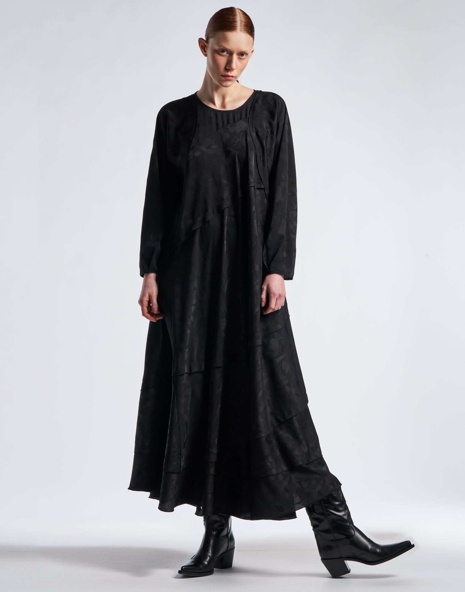 Frontalansicht: Modell trägt das Maxi-Kleid FAVOURITE aus schwarzem Funktionssatin mit floralem Damastmuster, ausgestelltem Rock, langen Ärmeln und Rundhalsausschnitt.