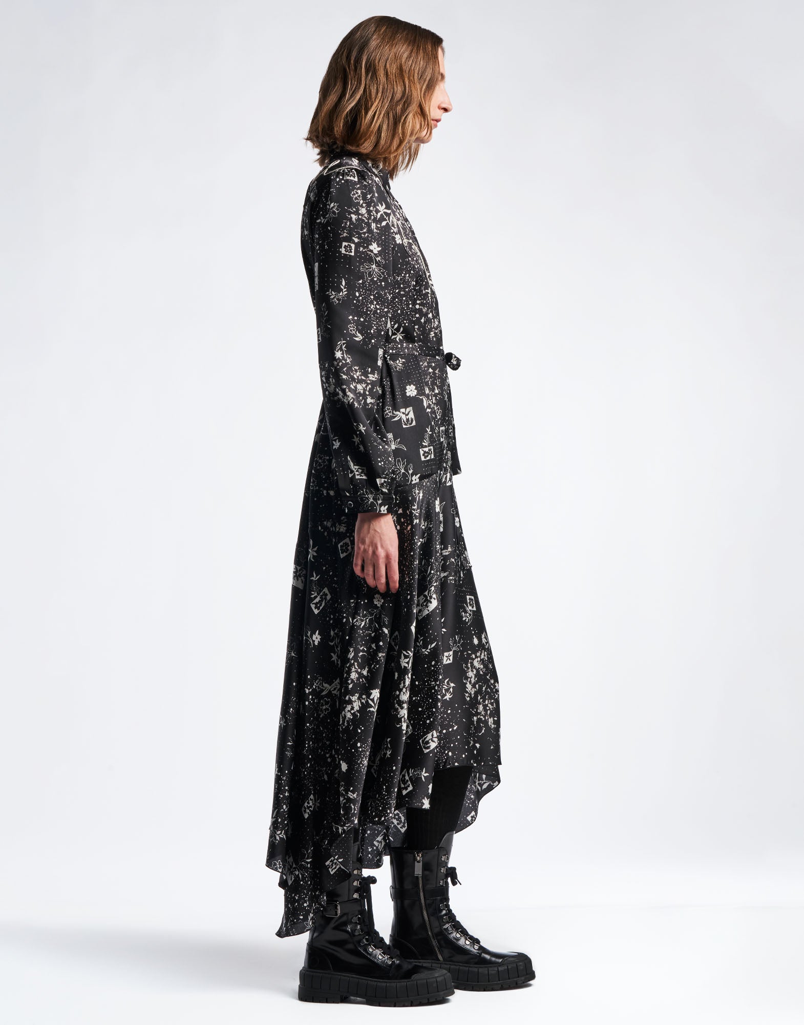 Side view of the COMPELLING shirtdress in black technical satin with geometric floral pattern and ivory accents, featuring a loose flared skirt and long sleeves.